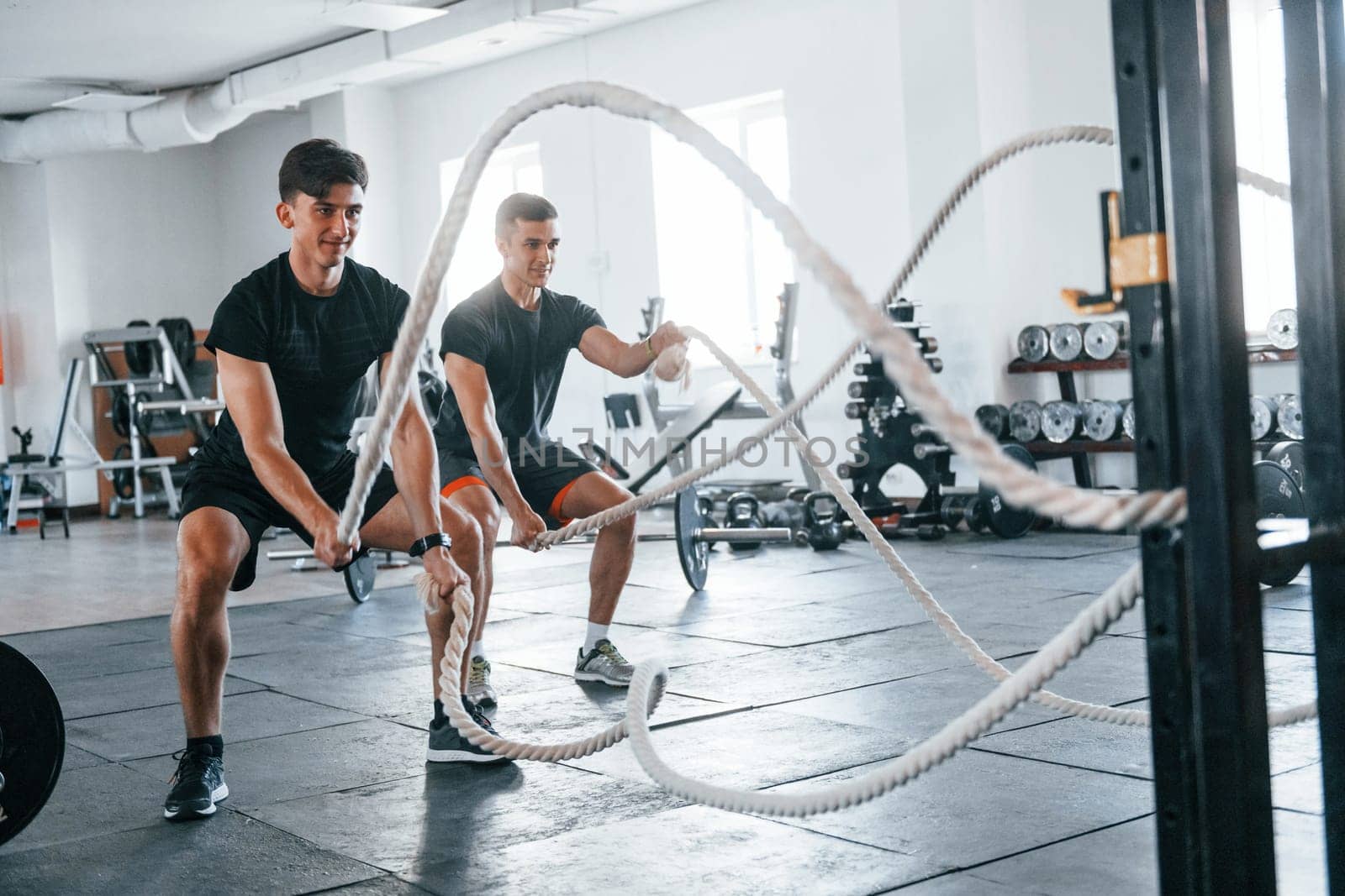 Young people with sportive body shapes doing crossfit by using knots.