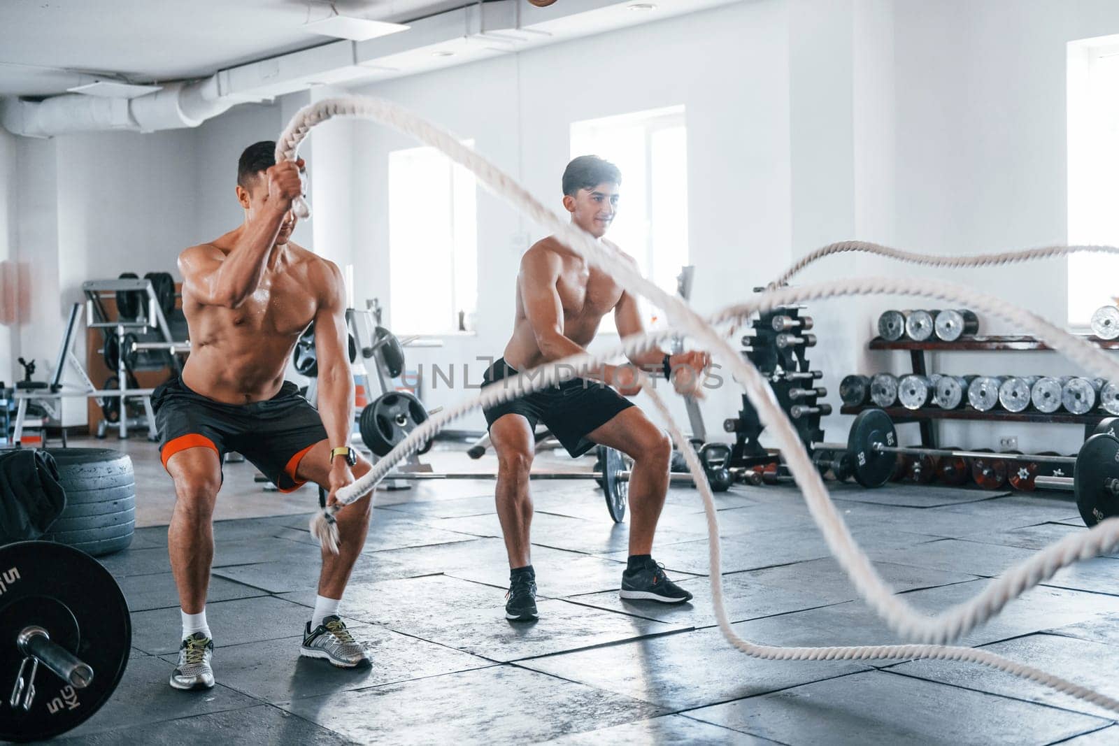 Young people with sportive body shapes doing crossfit by using knots.