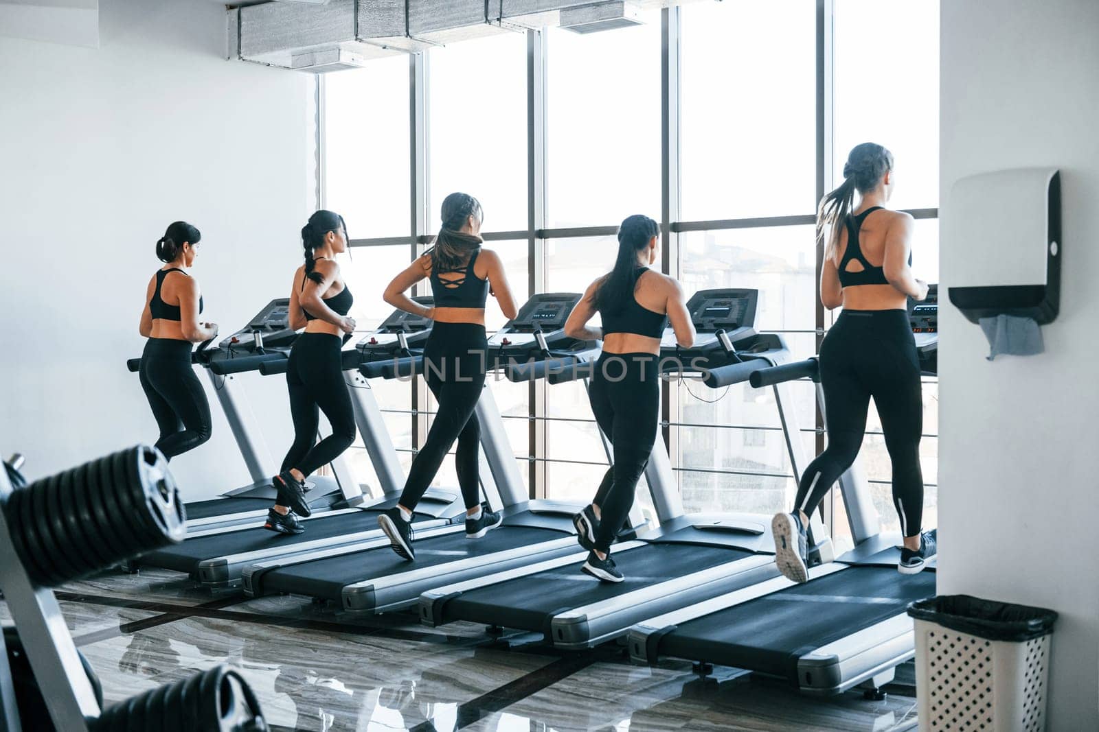 Running on a treadmill. Group of young sportive people have crossfit day indoors in gym.