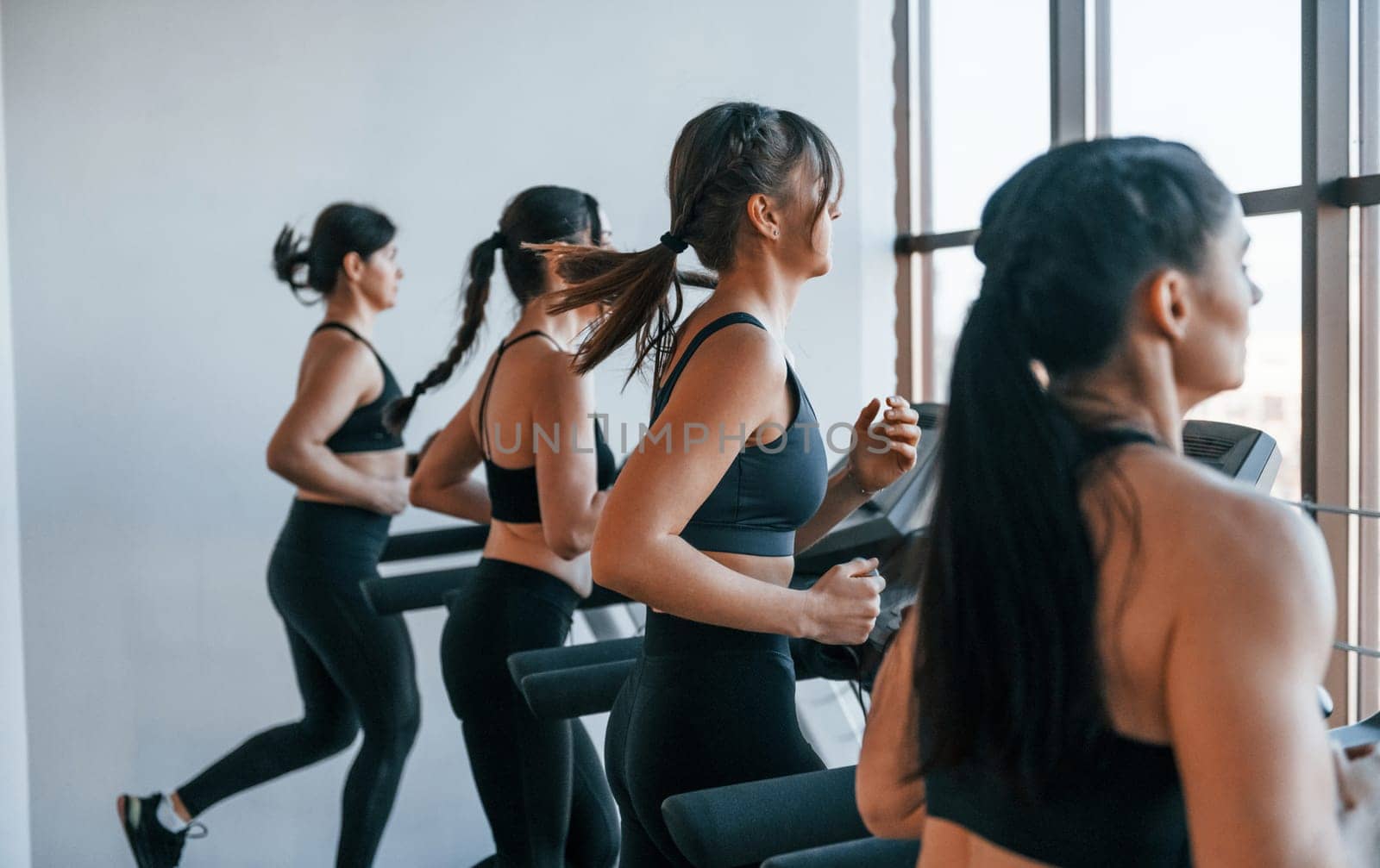 Running on a treadmill. Group of young sportive people have crossfit day indoors in gym.