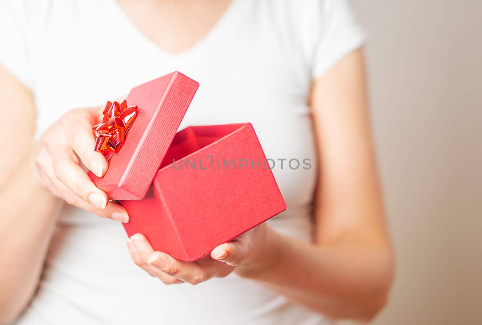 Valentine gift. Female hands opening a small gift in a red box with a heart.