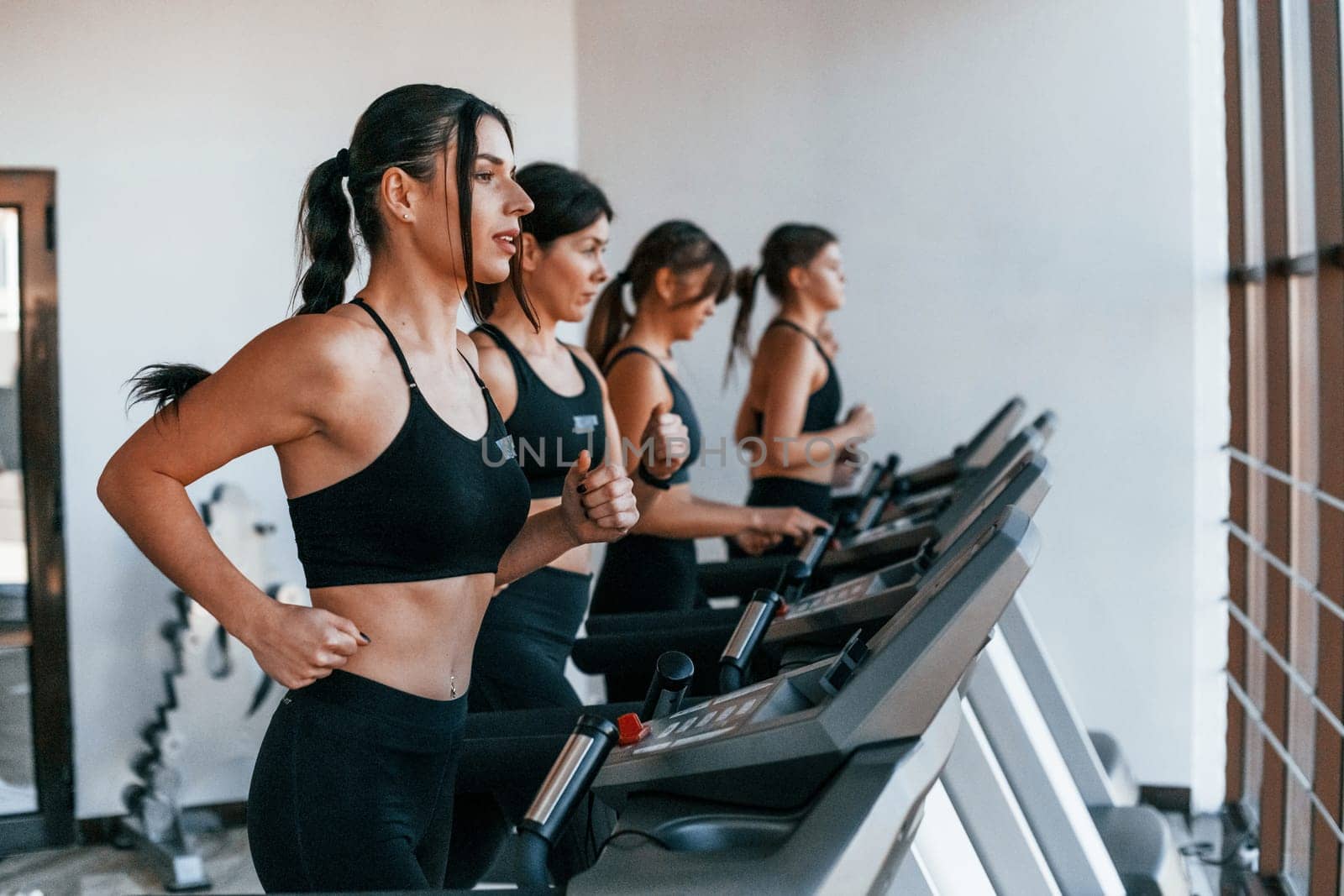 Running on a treadmill. Group of young sportive people have crossfit day indoors in gym.