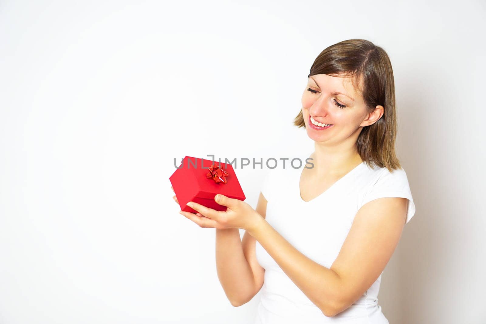 Happy pretty young woman in a white shirt holding a red gift box on the white background. High quality photo.