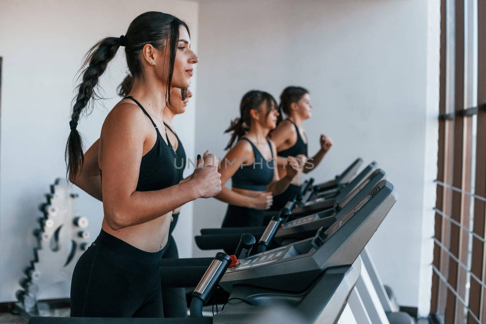 Running on a treadmill. Group of young sportive people have crossfit day indoors in gym.