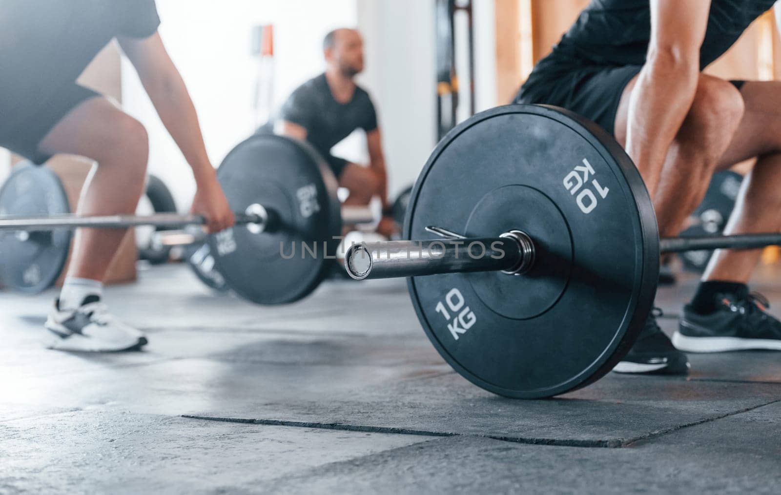 By using heavy weights. Group of young sportive people have crossfit day indoors in gym.