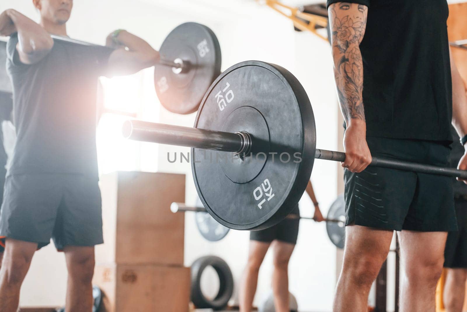 Lifting barbell. Group of young sportive people have crossfit day indoors in gym.
