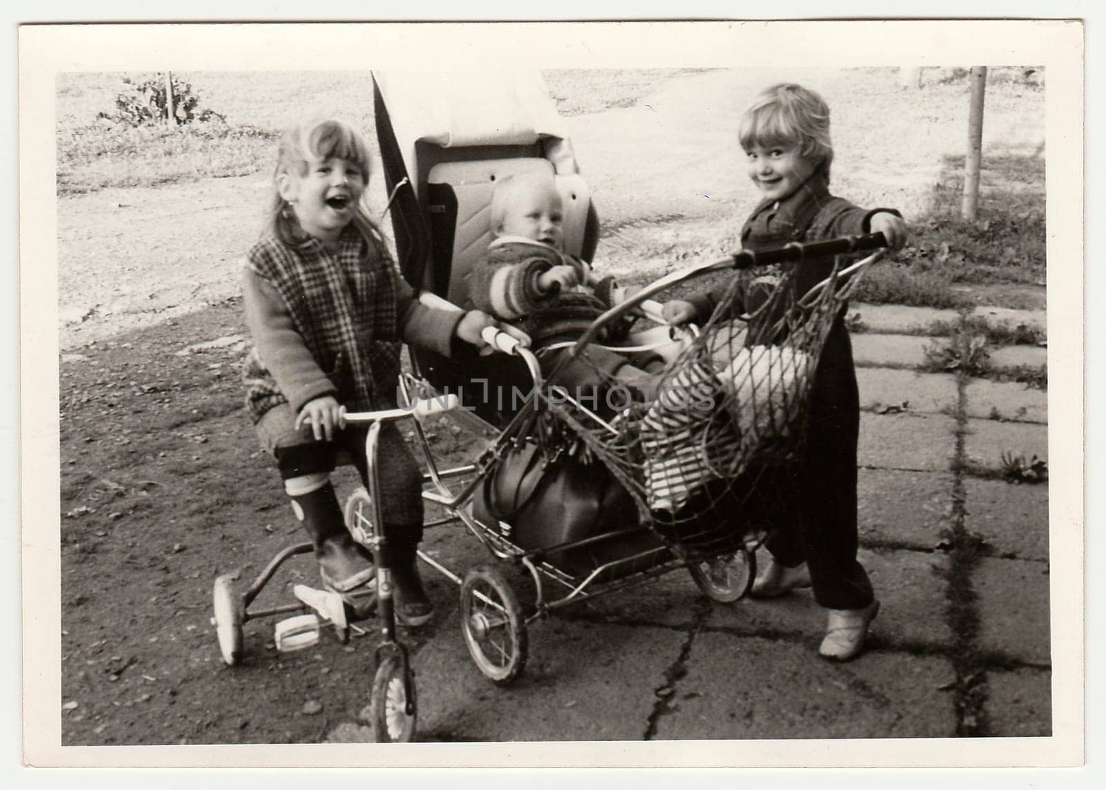 THE CZECHOSLOVAK SOCIALIST REPUBLIC - CIRCA 1970s: Retro photo shows children who play with pram and tricycle. Black and white vintage photography.