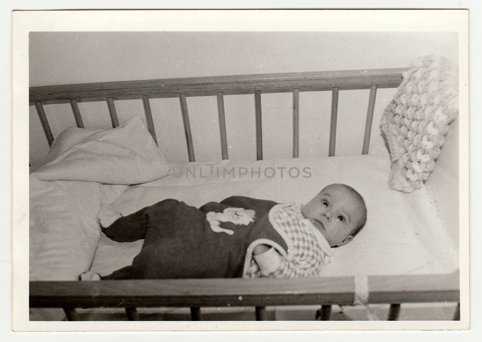Retro photo shows cute baby who lies in a bed. Black and white vintage photography. by roman_nerud