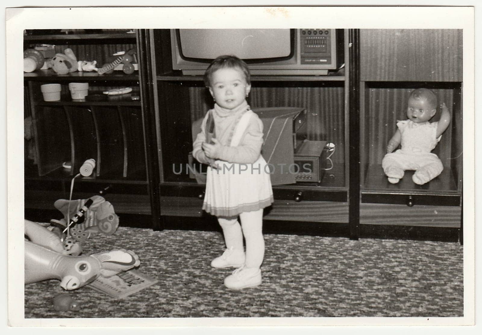 Retro photo shows child, girl who plays with toy. Black and white vintage photography. by roman_nerud