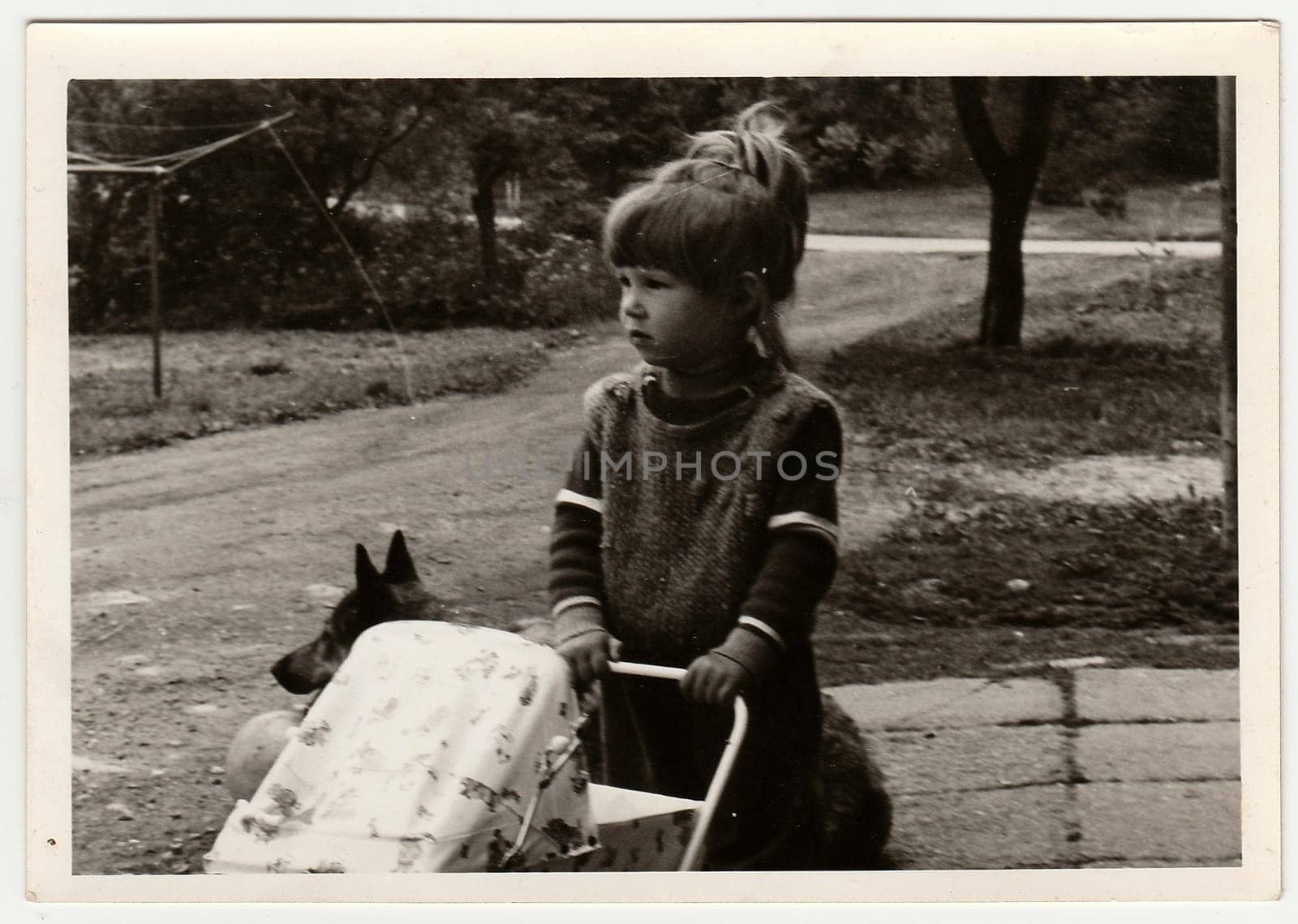 Retro photo shows child, girl who plays with toy - dolls pram. Black and white vintage photography. by roman_nerud