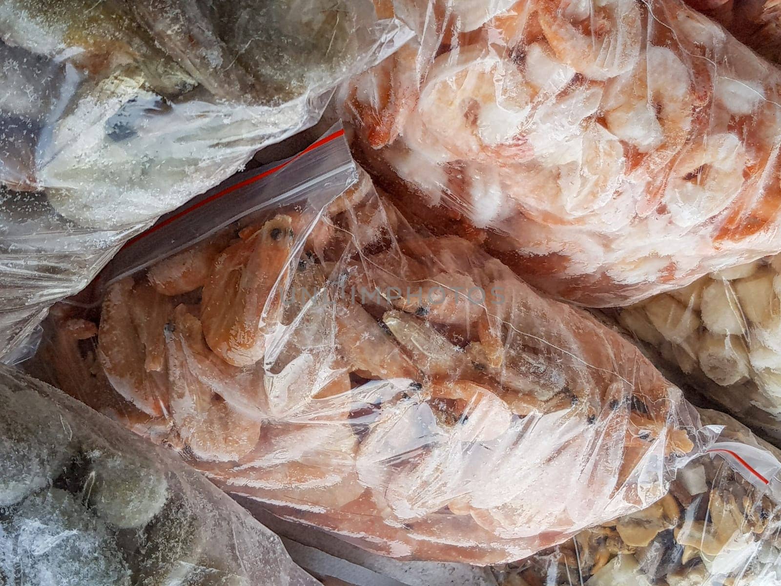 There are many large plastic bags with frozen raw and boiled shrimp on the counter of the fish market