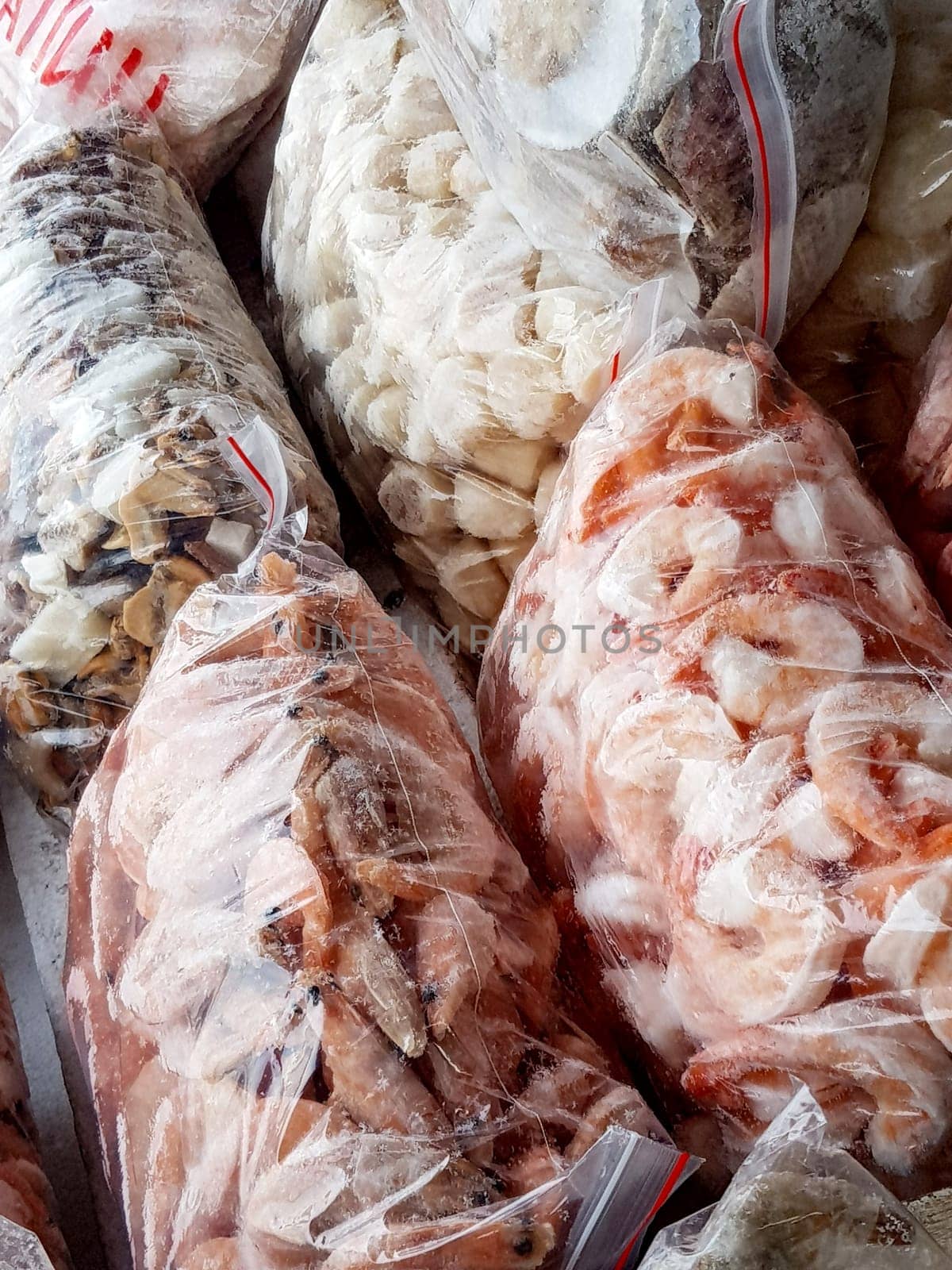 There are many large plastic bags with frozen raw and boiled shrimp on the counter of the fish market