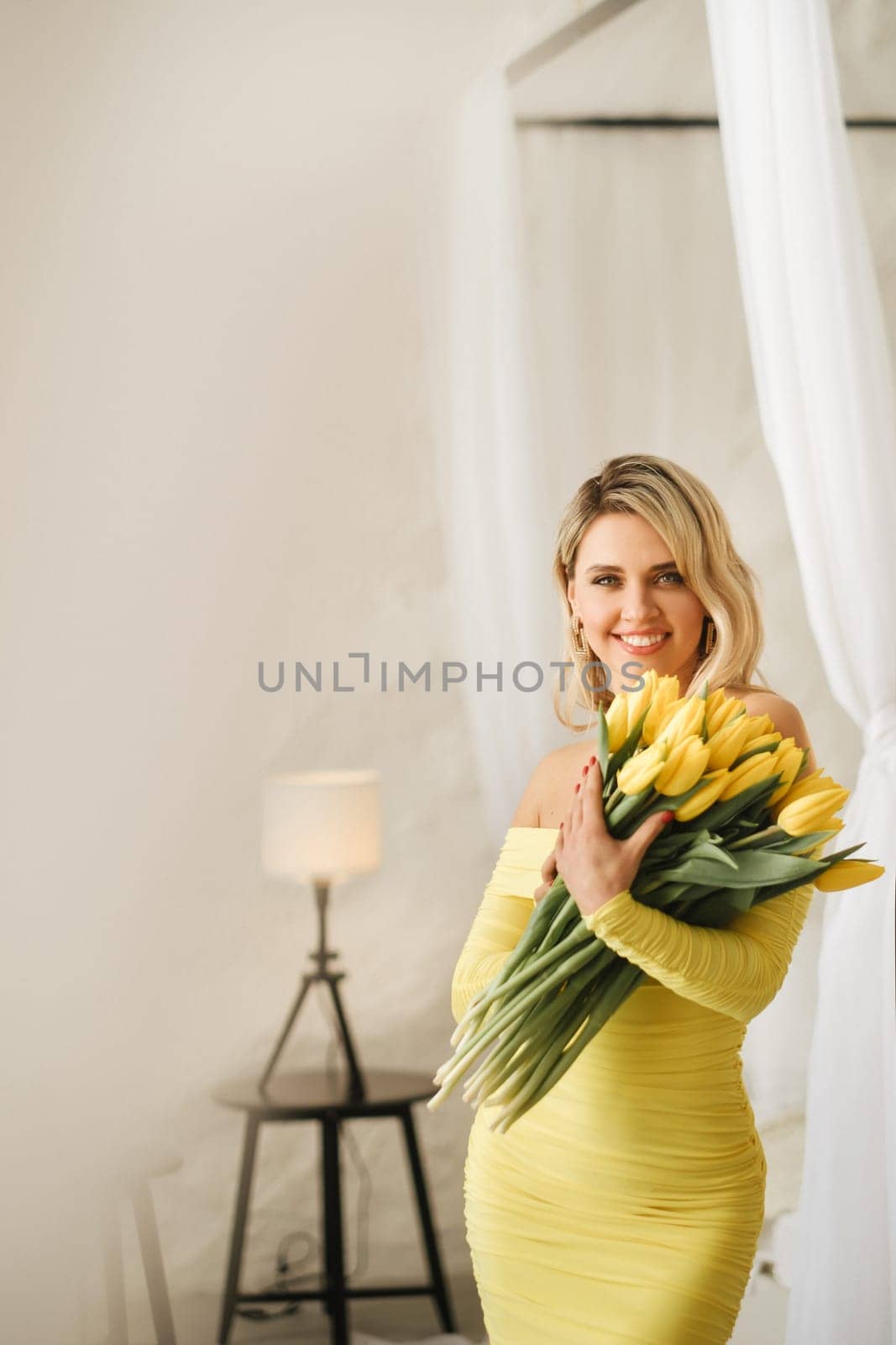 a happy woman in a yellow dress embraces a bouquet of yellow spring tulips in the interior.