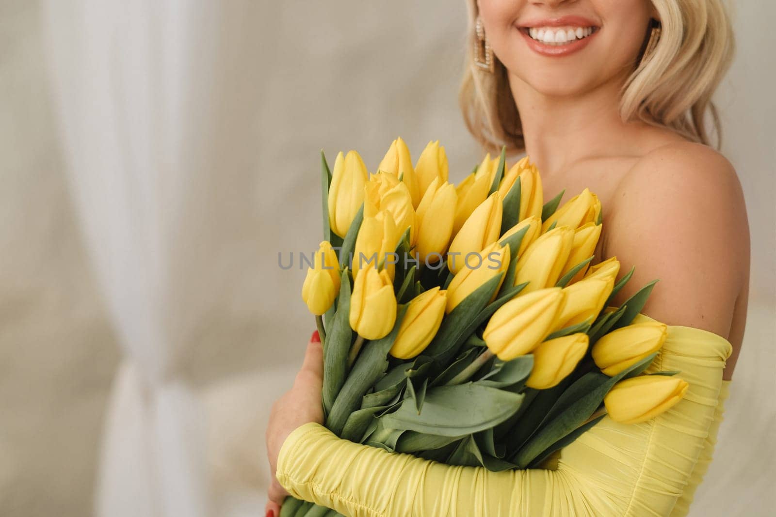 a happy woman in a yellow dress embraces a bouquet of yellow spring tulips in the interior.