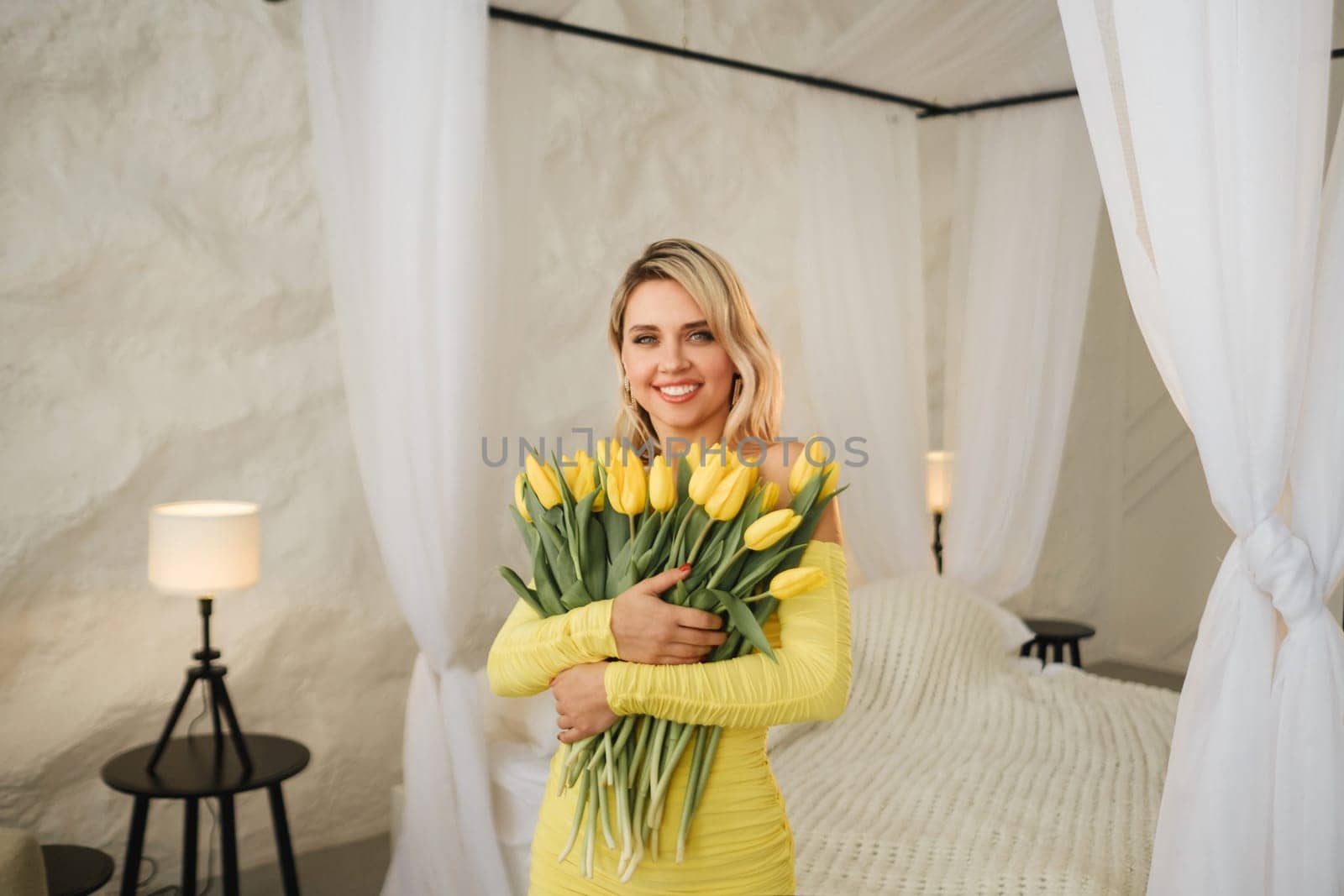 a happy woman in a yellow dress embraces a bouquet of yellow spring tulips in the interior.