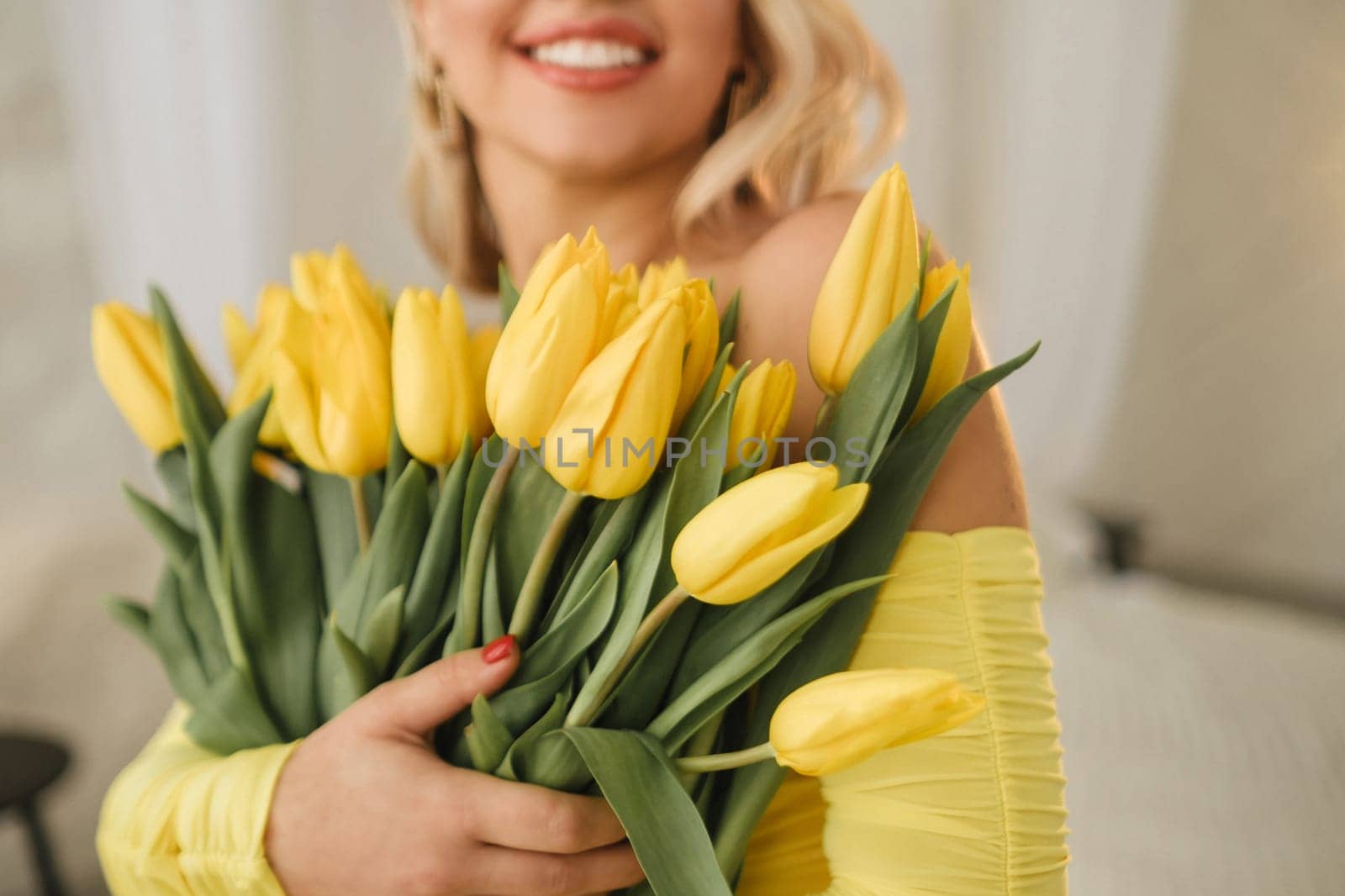 a happy woman in a yellow dress embraces a bouquet of yellow spring tulips in the interior.