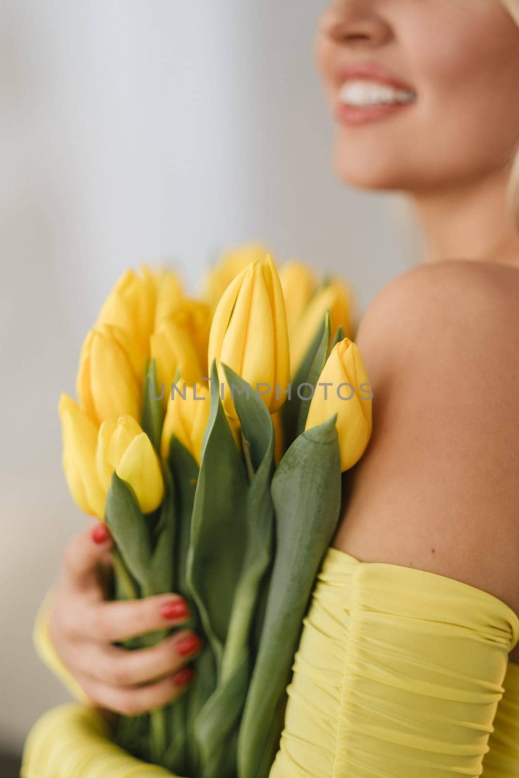 a happy woman in a yellow dress embraces a bouquet of yellow spring tulips in the interior by Lobachad