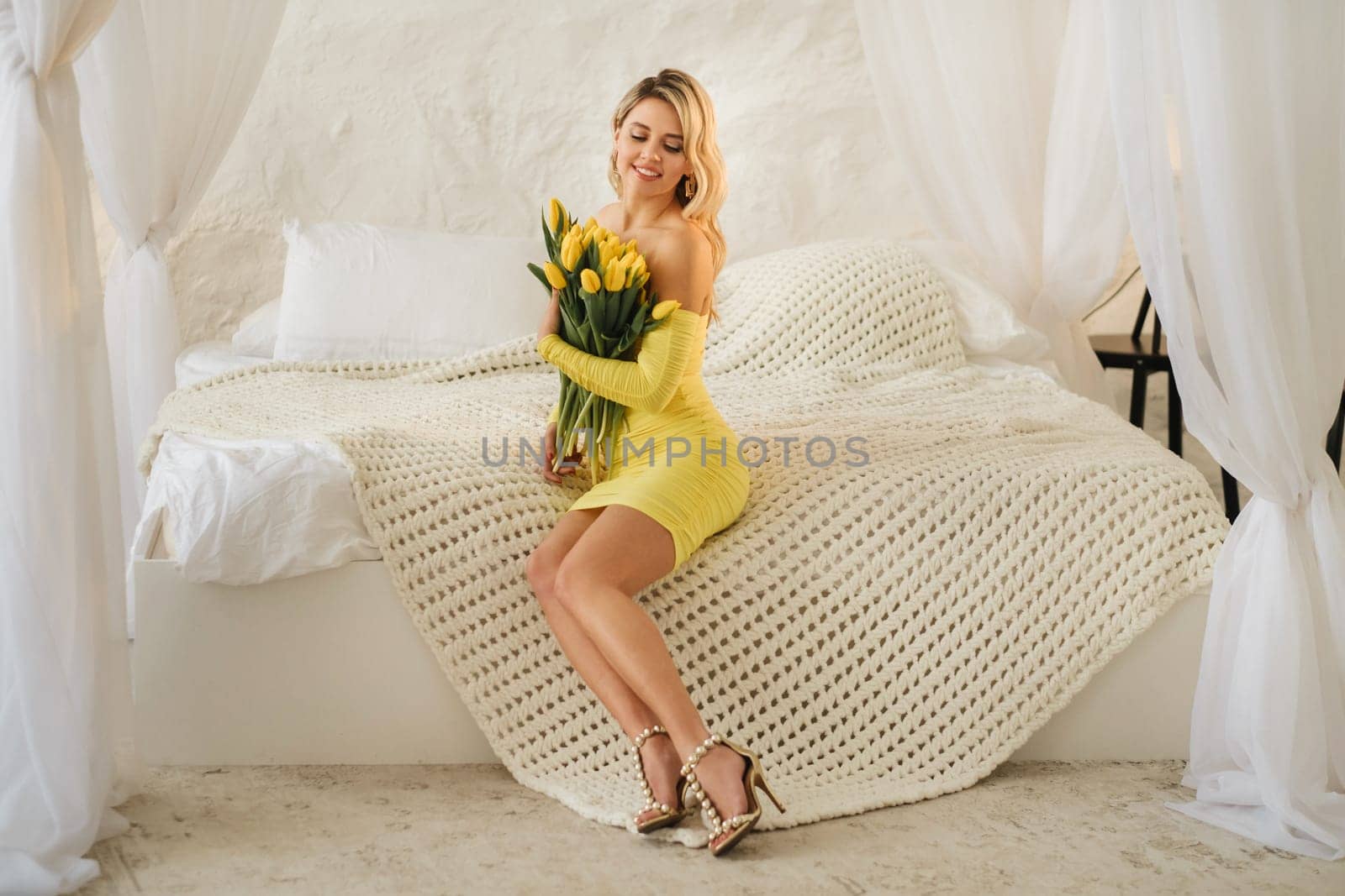 a happy woman in a yellow dress embraces a bouquet of yellow spring tulips in the interior.