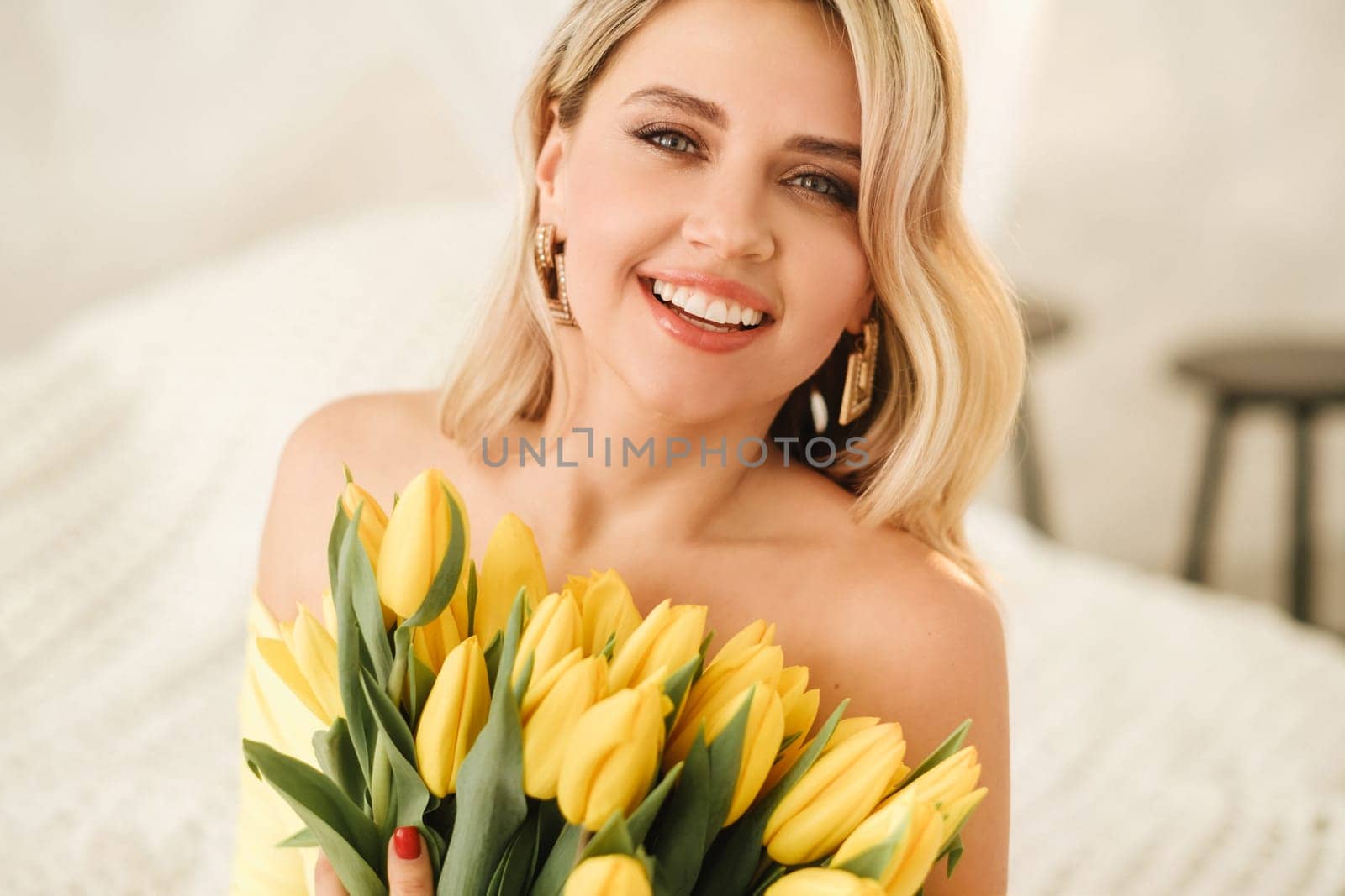 a happy woman in a yellow dress embraces a bouquet of yellow spring tulips in the interior.