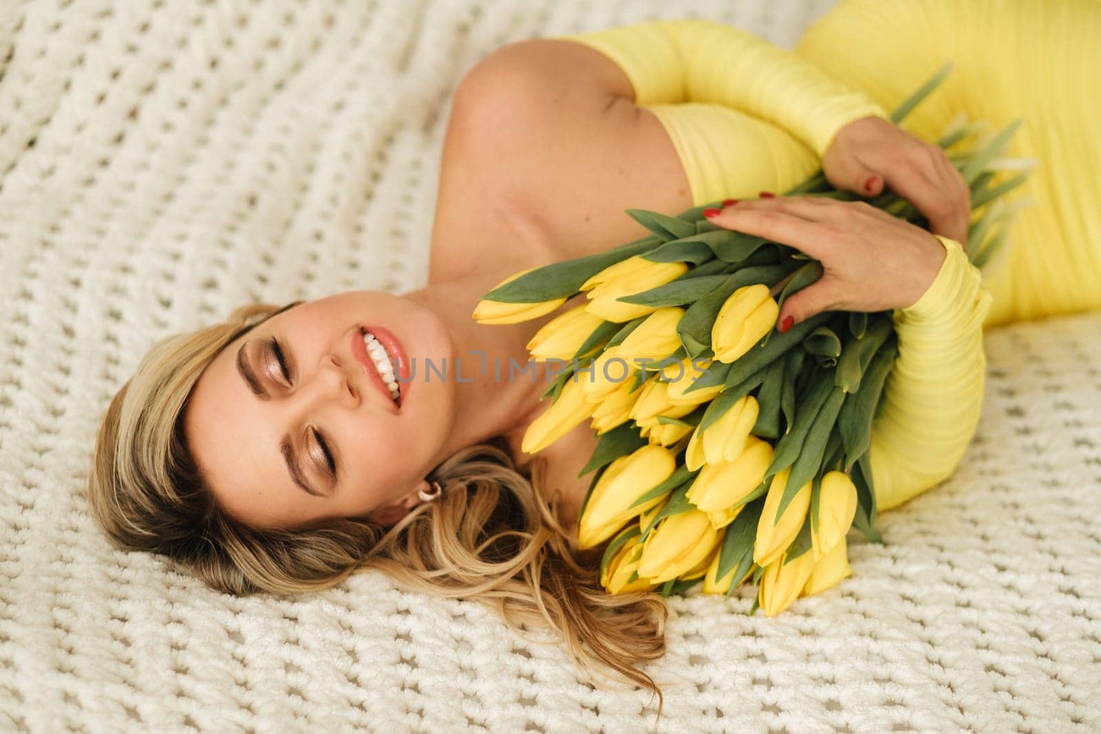 a happy woman in a yellow dress embraces a bouquet of yellow spring tulips in the interior.