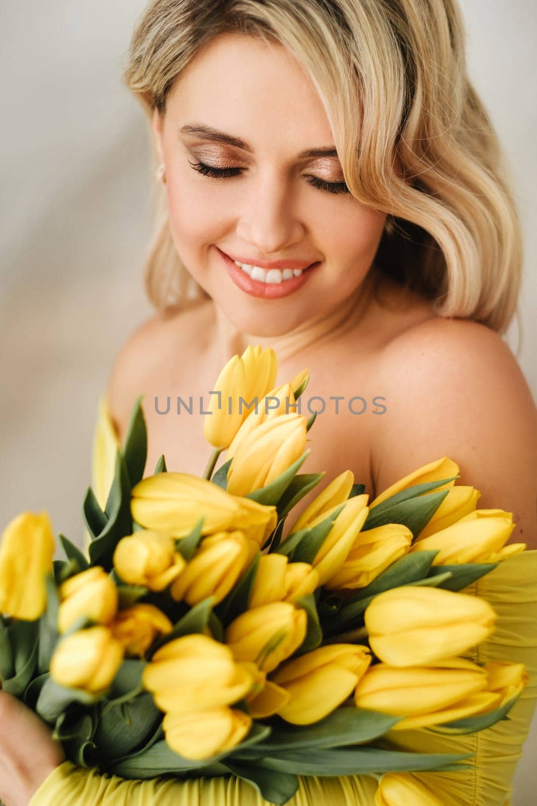 a happy woman in a yellow dress embraces a bouquet of yellow spring tulips in the interior by Lobachad