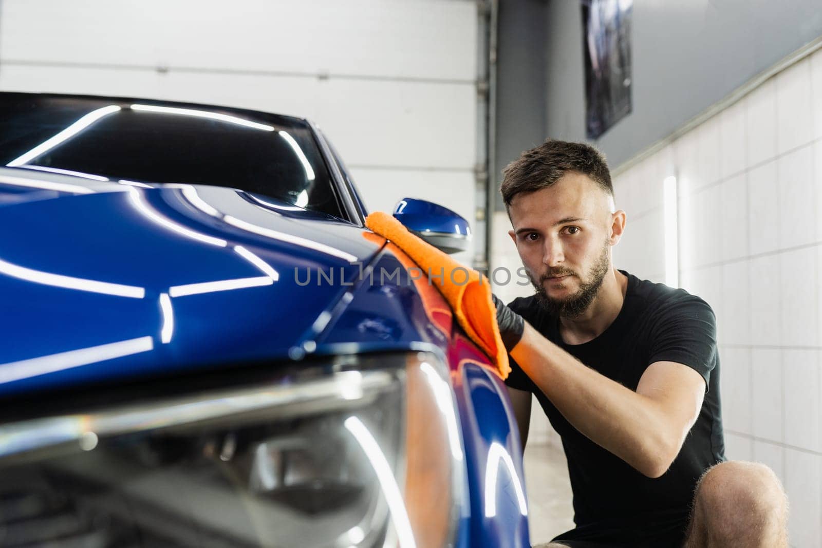 Hand car drying with microfiber in detailing auto service. Cleaner worker dry body car after washing automobile. by Rabizo