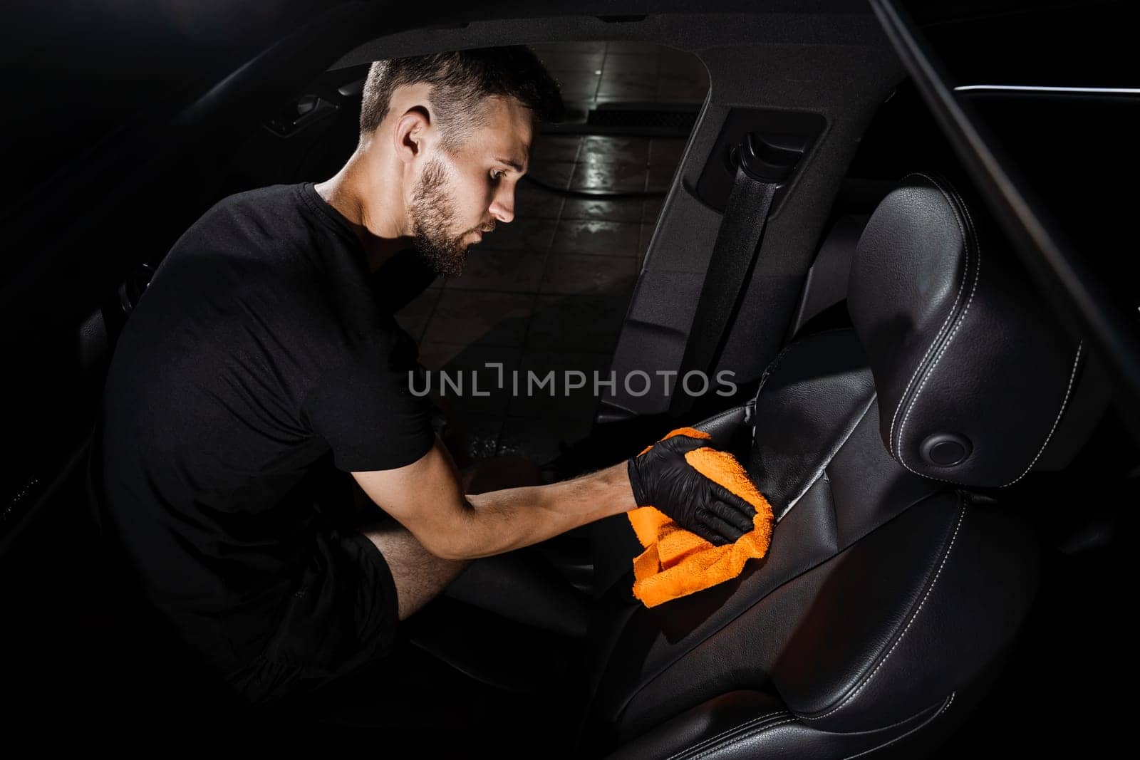 Hand car interior drying of leather seat using microfiber in detailing auto service. Cleaner worker dry car interior