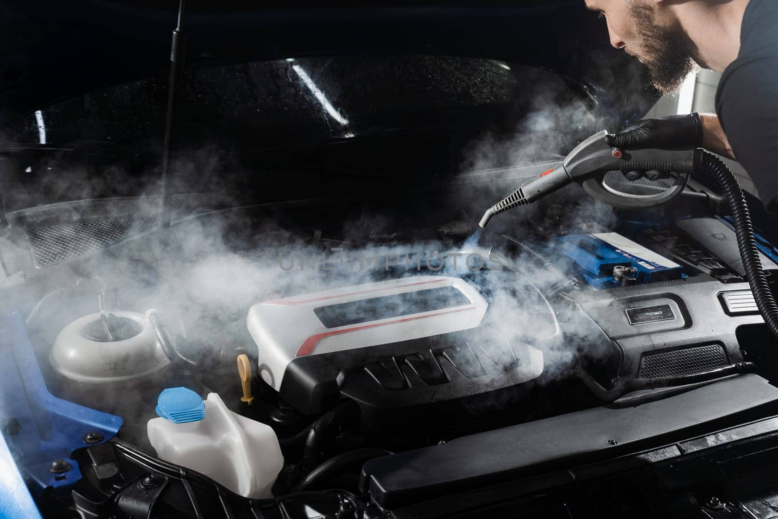 Process of steam cleaning car engine from dust and dirt. Steaming washing of motor of auto in detailing auto service