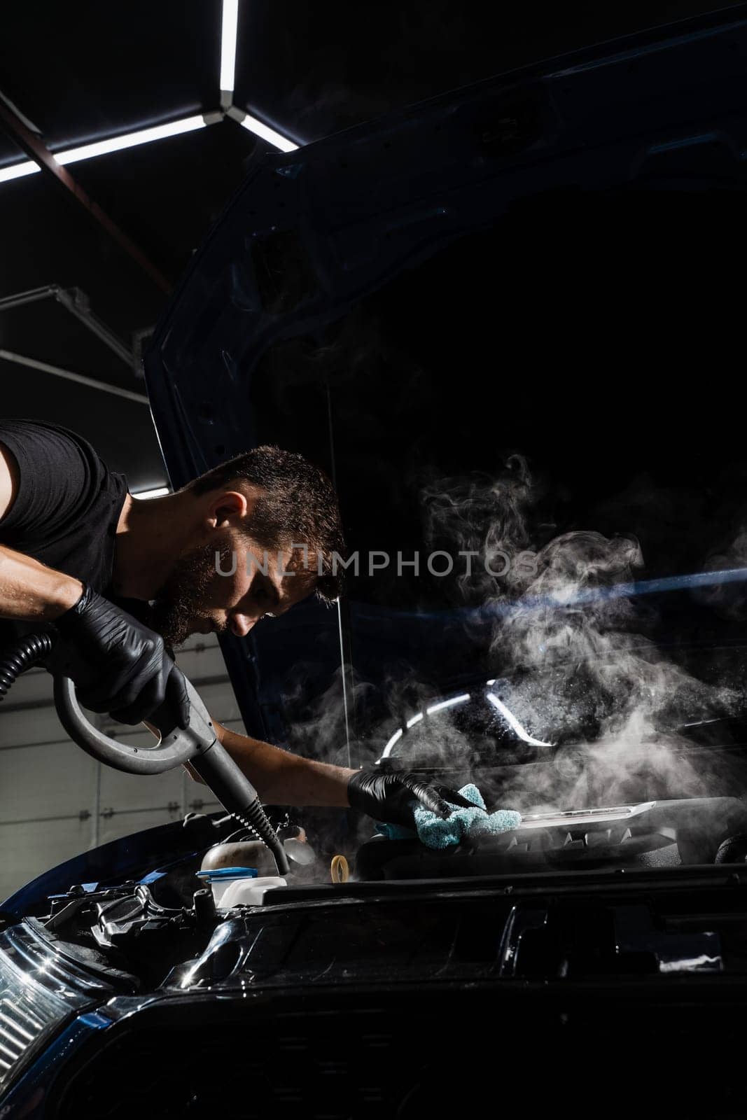 Process of steam cleaning car engine from dust and dirt. Steaming washing of motor of auto in detailing auto service