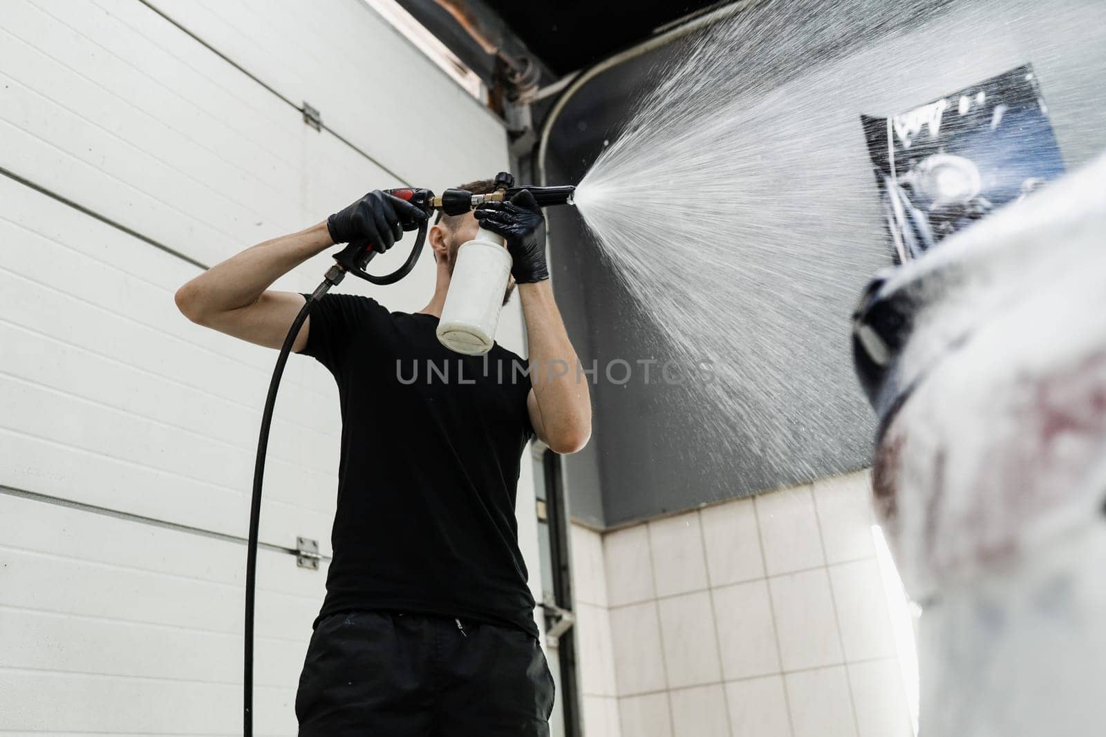 Second phase of detailing washing in car service. Car washer does full body car wash. Process of spraying foam on the car body in the garage. by Rabizo