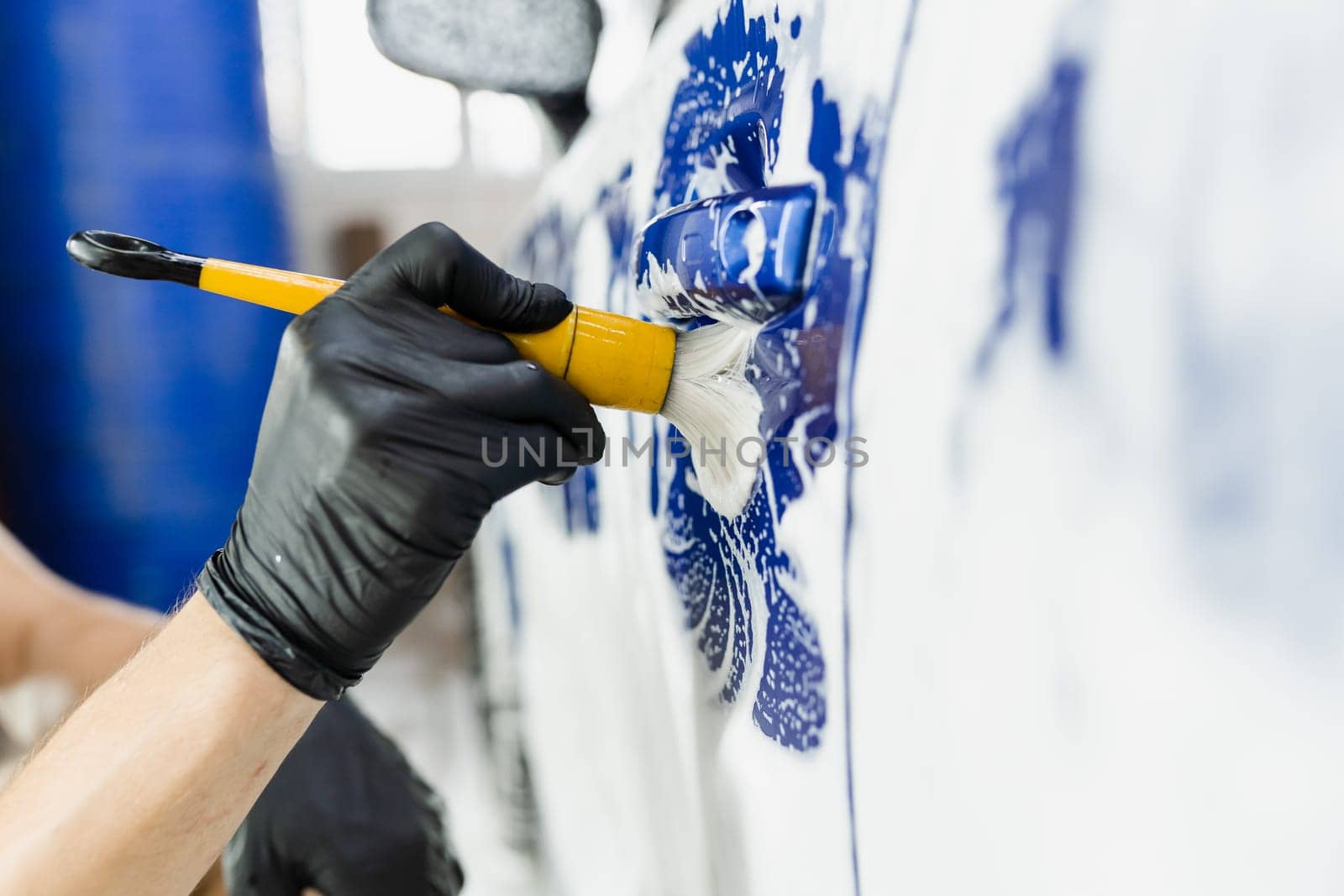 Hand brush washing of car body with foam in car detailing service. Car wash worker washes a car body