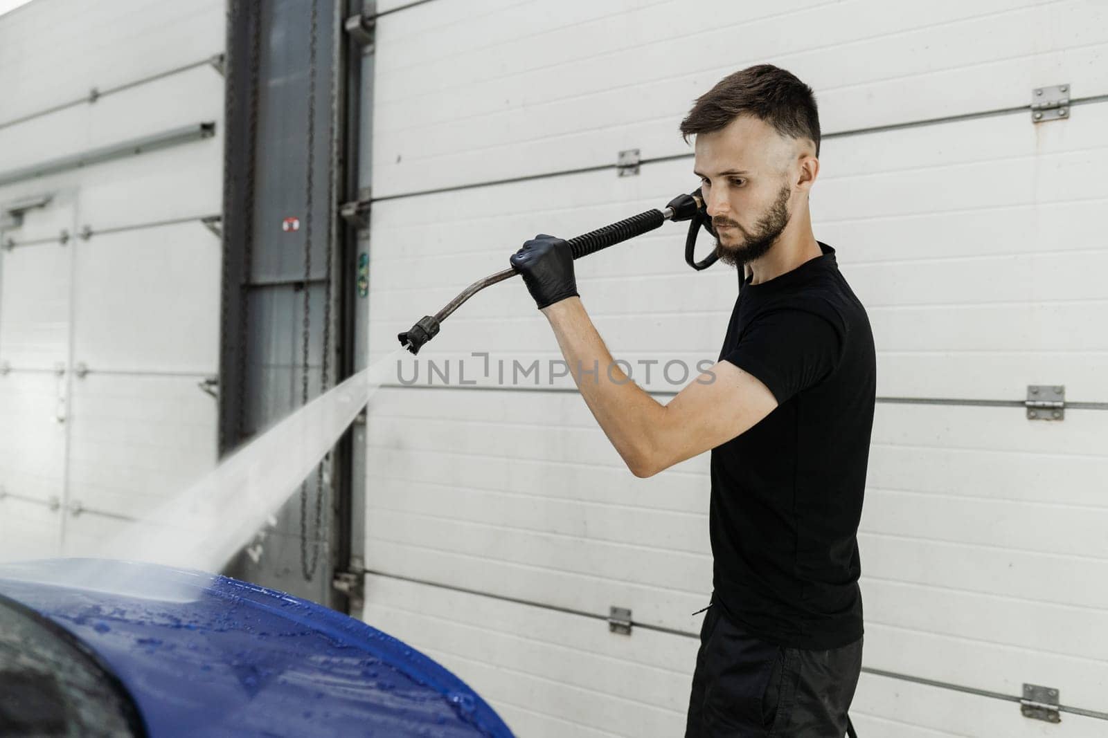 Spraying water on car to wash off foam in the garage. Process of detailing washing in car service. Car washer pouring water for full body car wash