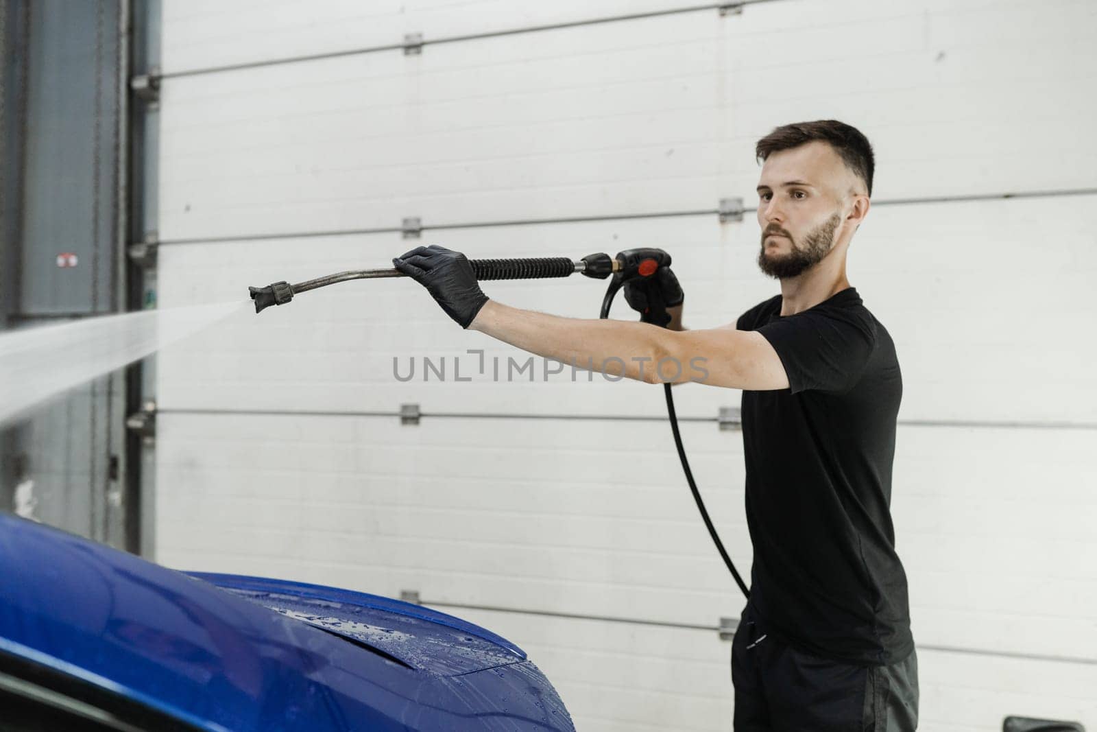 Spraying water on car to wash off foam in the garage. Process of detailing washing in car service. Car washer pouring water for full body car wash