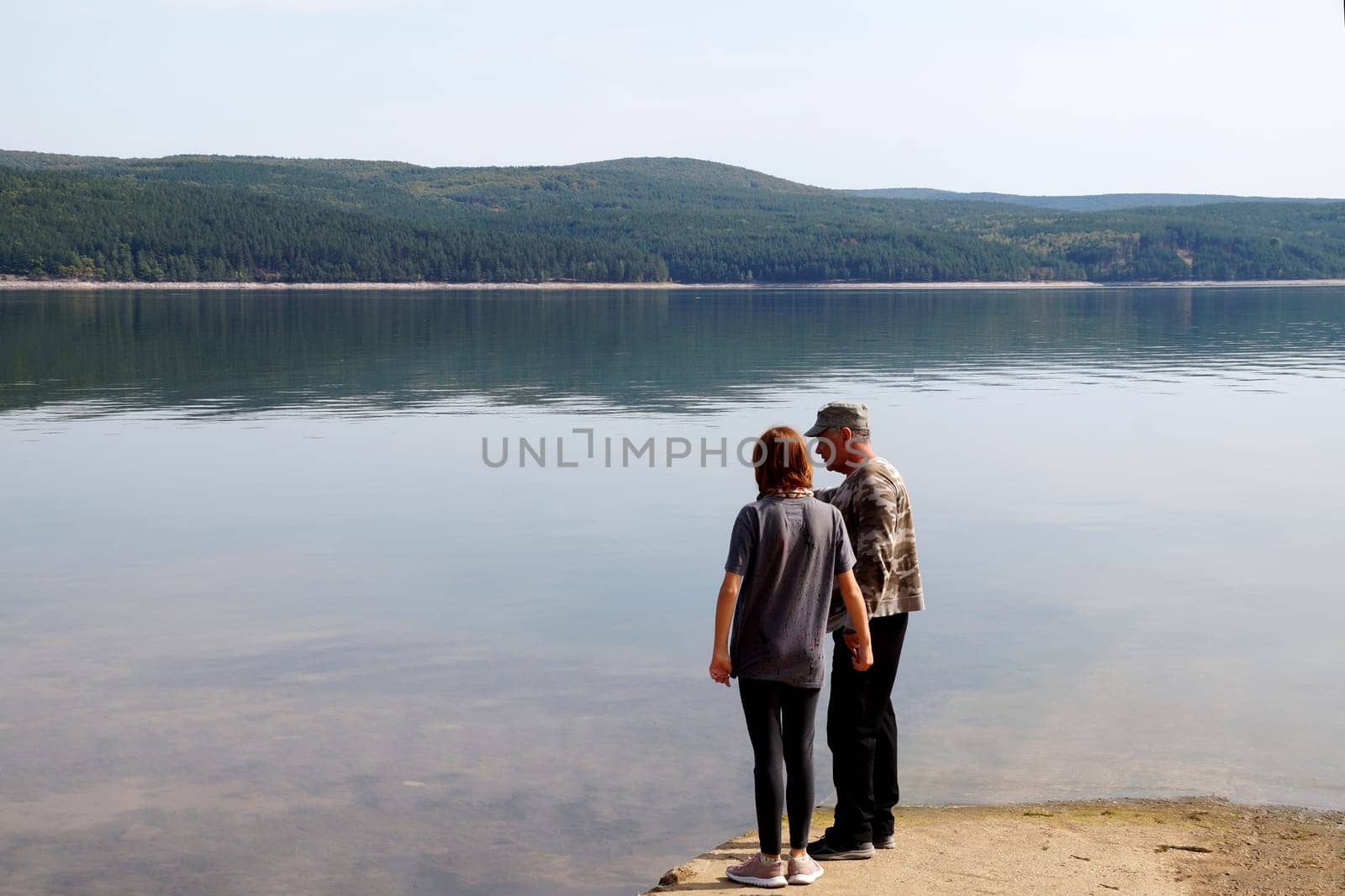 a teenage girl with her father are standing on the shore of a beautiful forest lake.