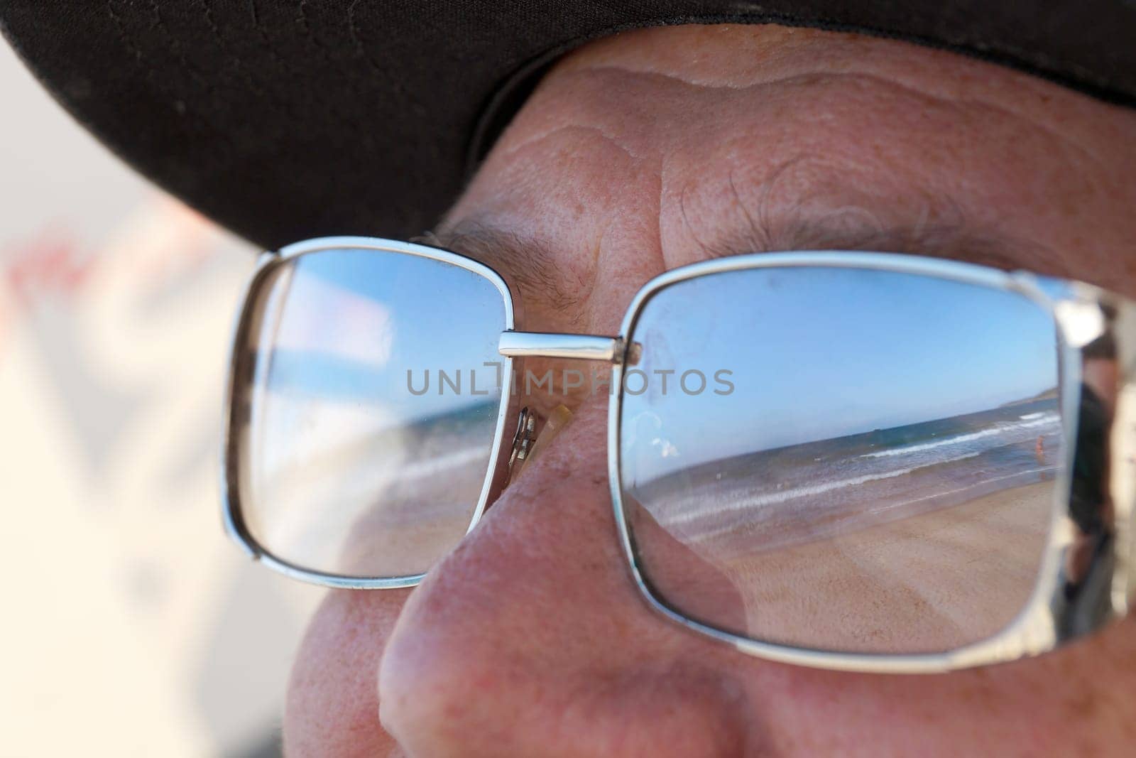 the beach and the sea are reflected in the man's sunglasses by Annado