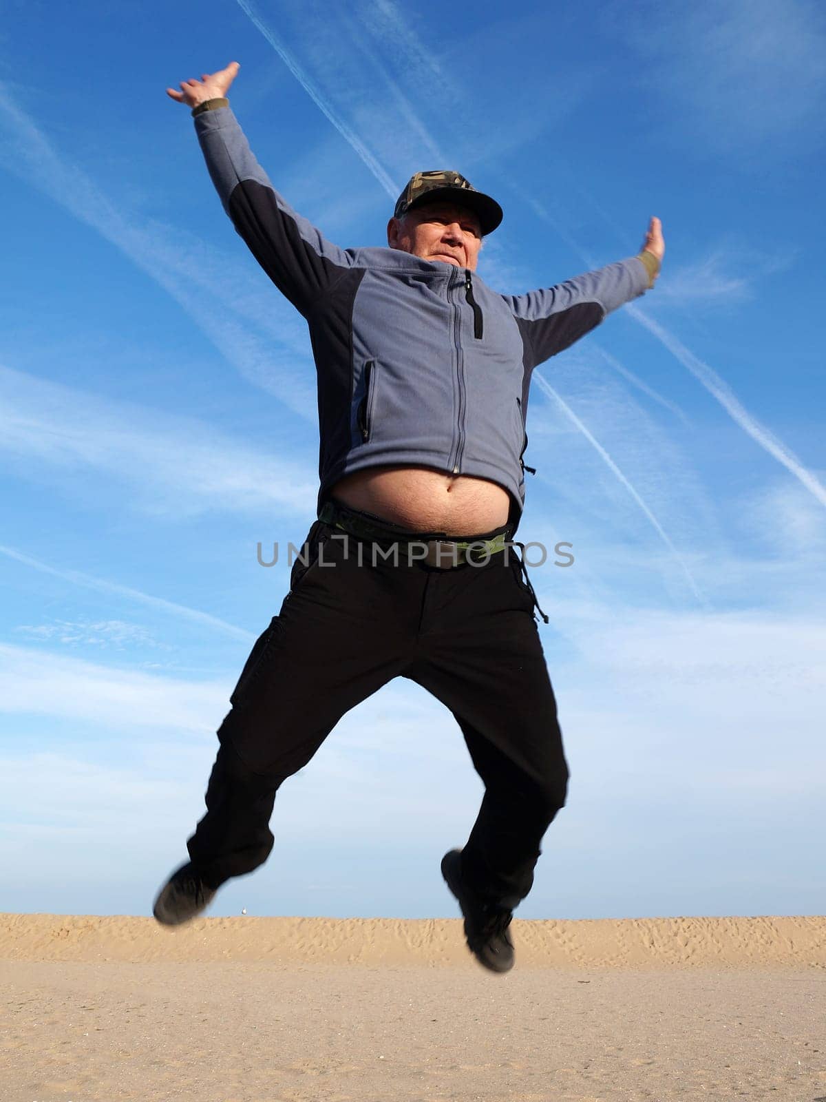 adult man jumping with his arms outstretched against the sky by Annado