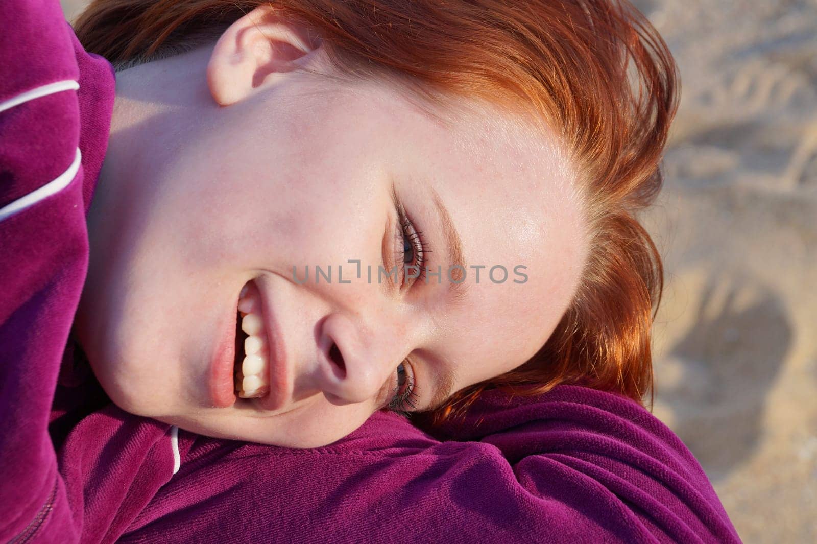 portrait of a smiling red-haired teenage girl lying on the sand, close-up