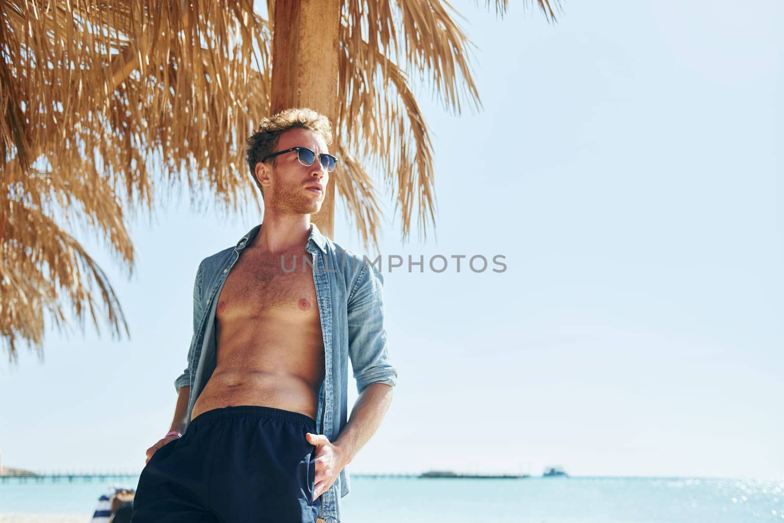 Posing for a camera. Young european man have vacation and enjoying free time on the beach of sea by Standret