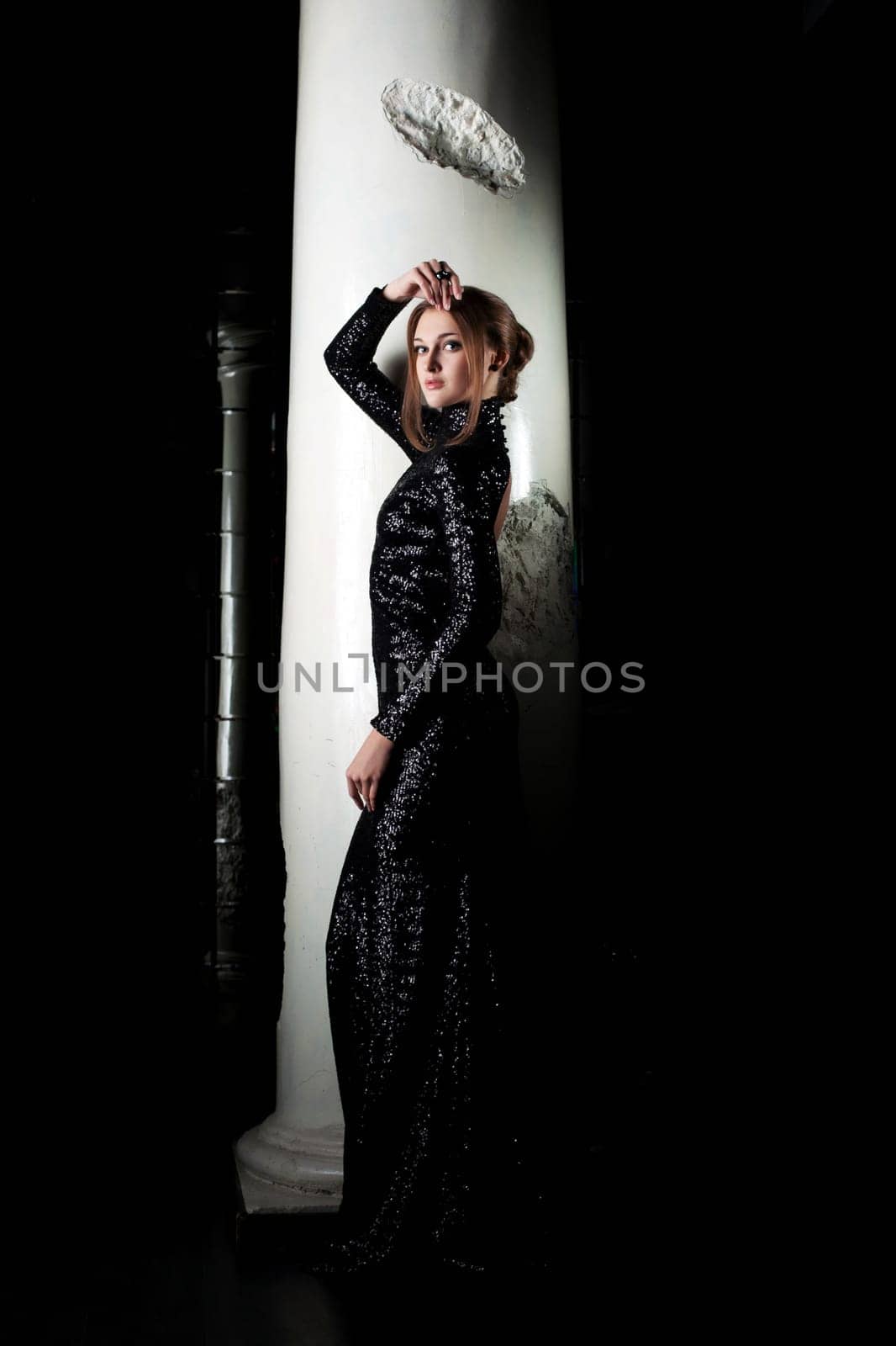 Attractive woman posing in black cocktail dress near column