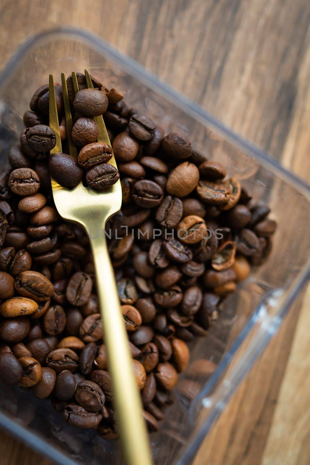 Roasted coffee bean in a plastic box along with a fork, close-up, top view. The concept of making coffee. by sfinks
