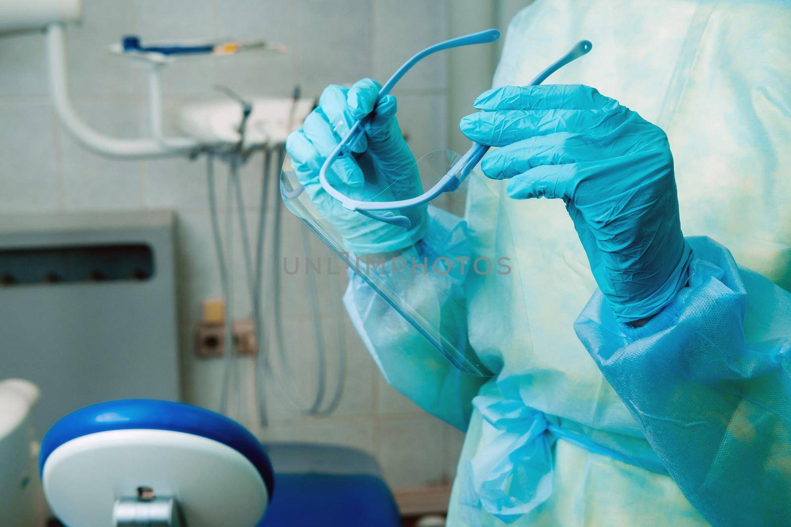 close up of a dentist's hands holding a protective plastic screen in his office by Lobachad