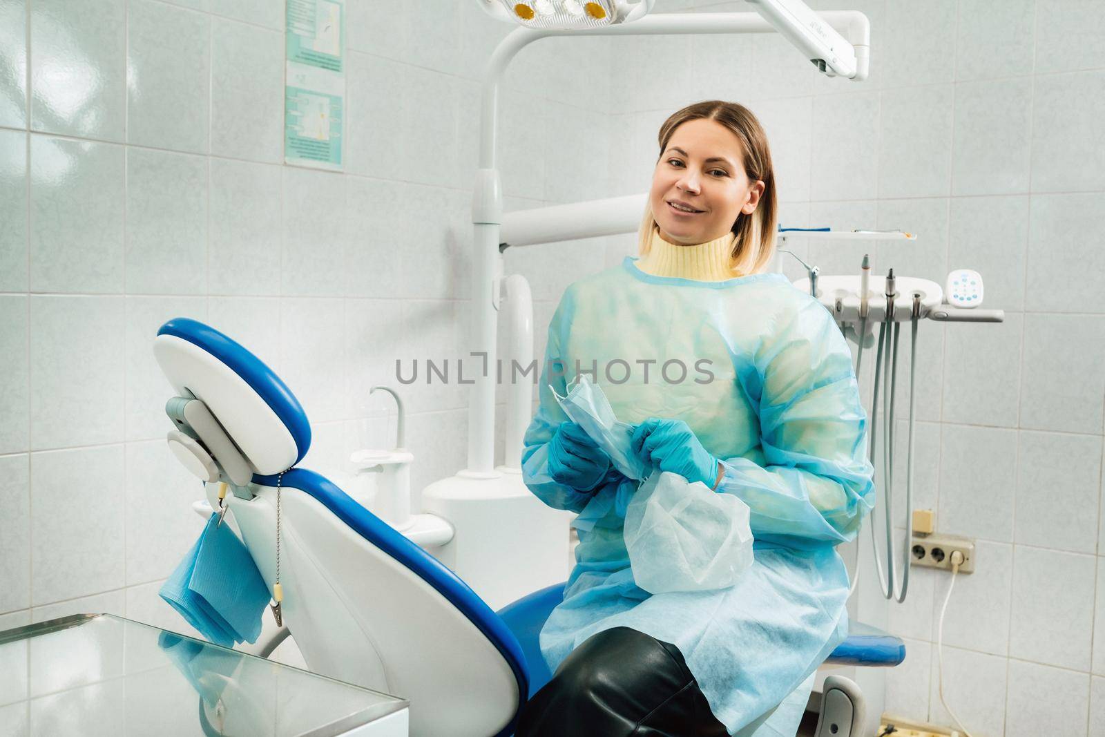 a female dentist with a medical mask and rubber gloves in her hands sits in her office.