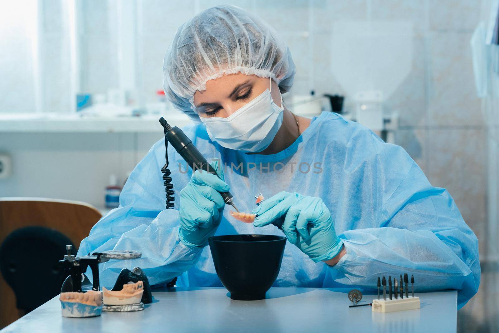 A masked and gloved dental technician works on a prosthetic tooth in his lab by Lobachad