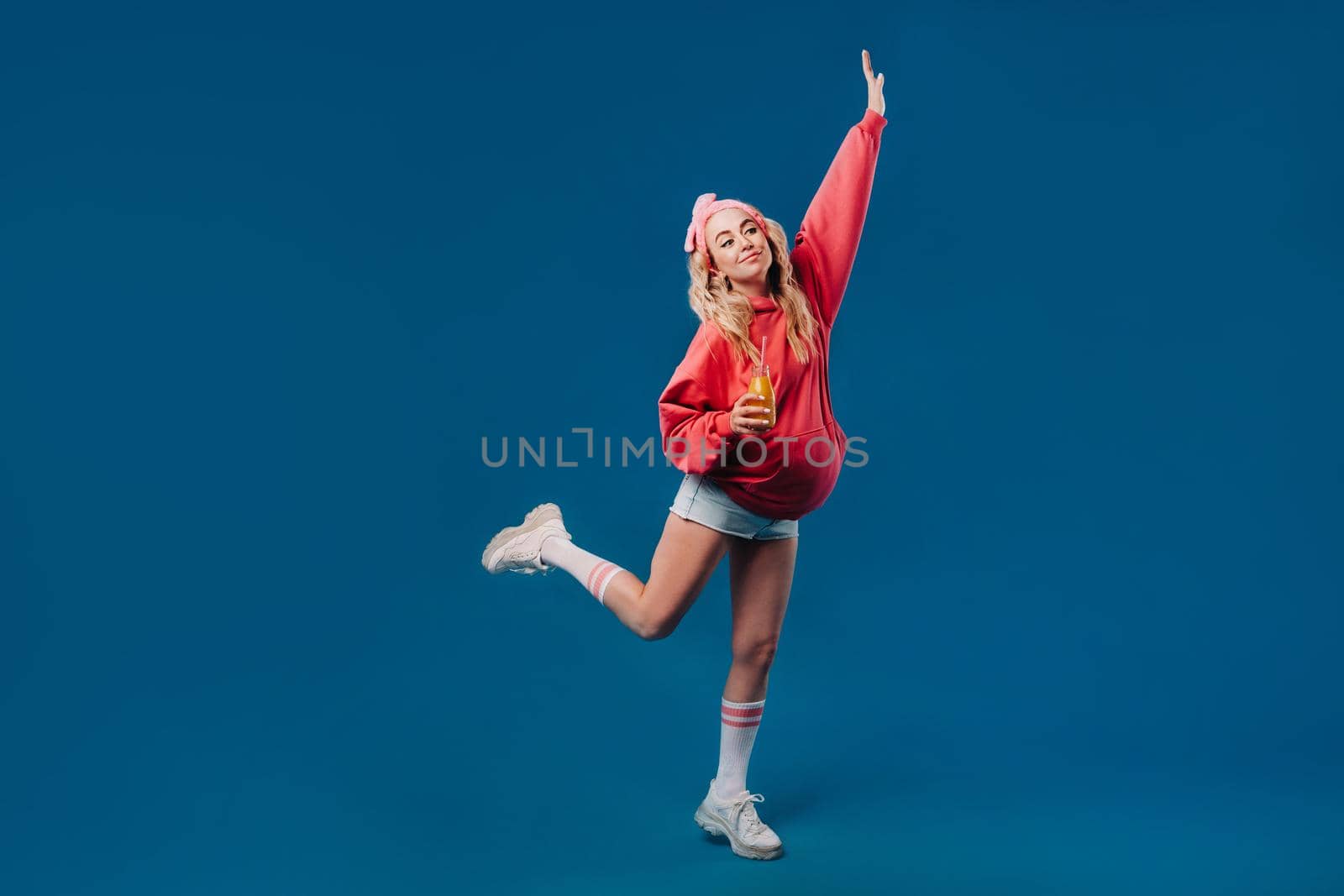 pregnant girl in pink clothes with a bottle of juice on a blue background.