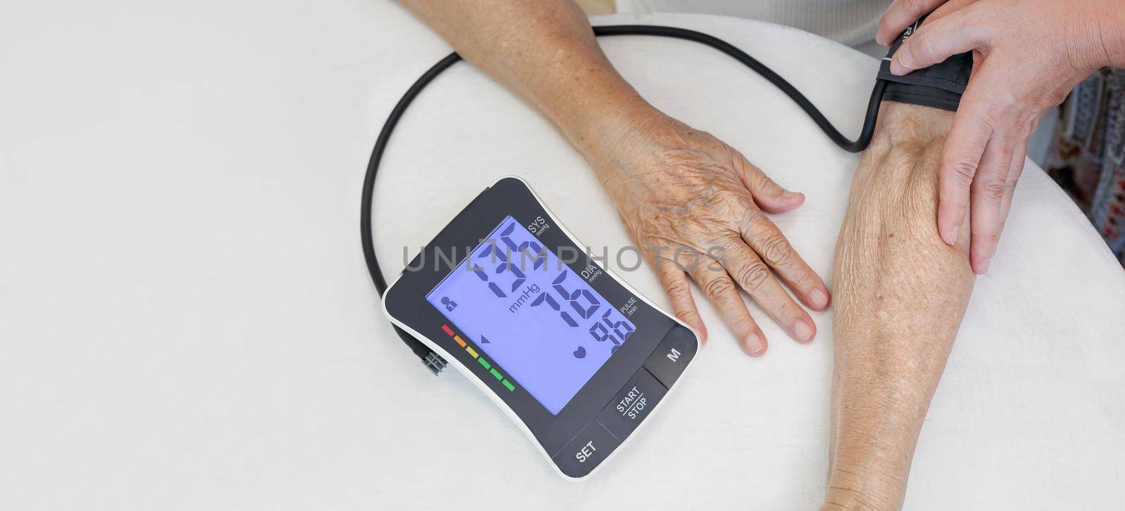 Daughter checking blood pressure (hypertension) of elderly mother at home