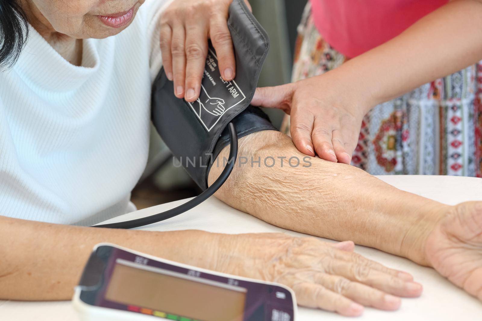 Daughter checking blood pressure (hypertension) of elderly mother at home by toa55
