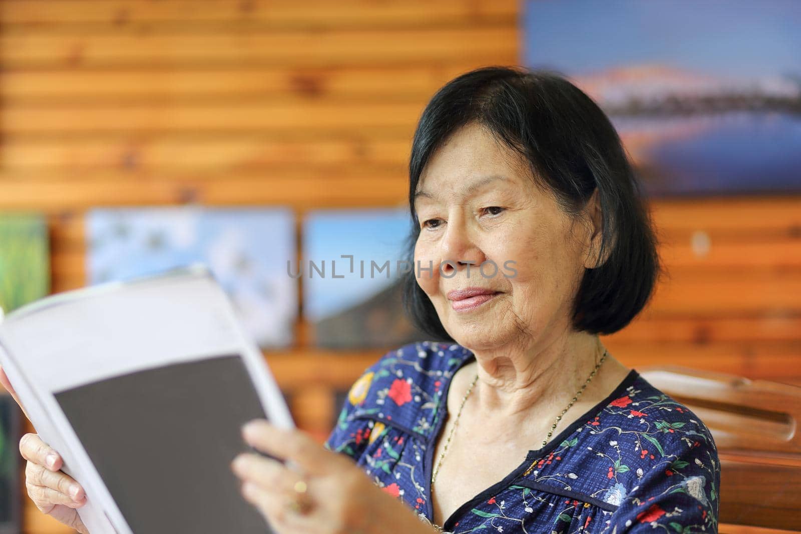 Elderly asian woman smiling while reading magazine