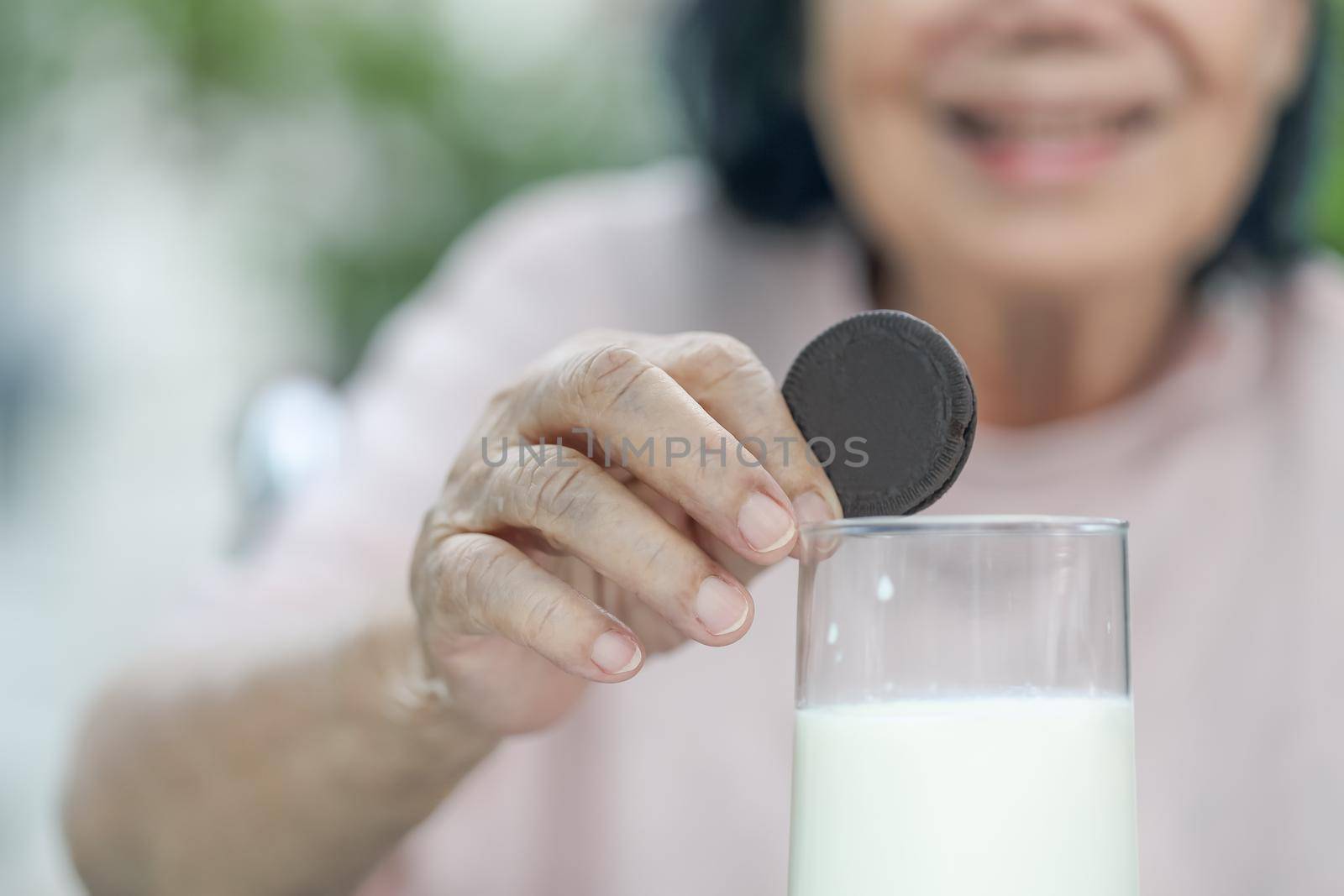 elderly hand dipping a chocolate cookie In milk glass by toa55
