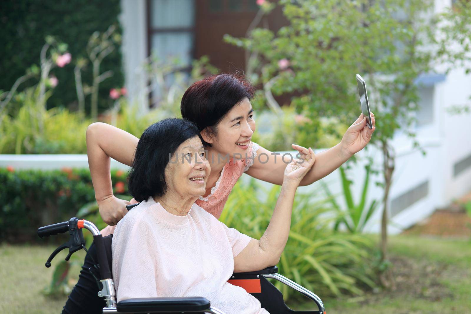 Daughter caring for the elderly asian woman ,do selfie, happy, smiles in backyard.