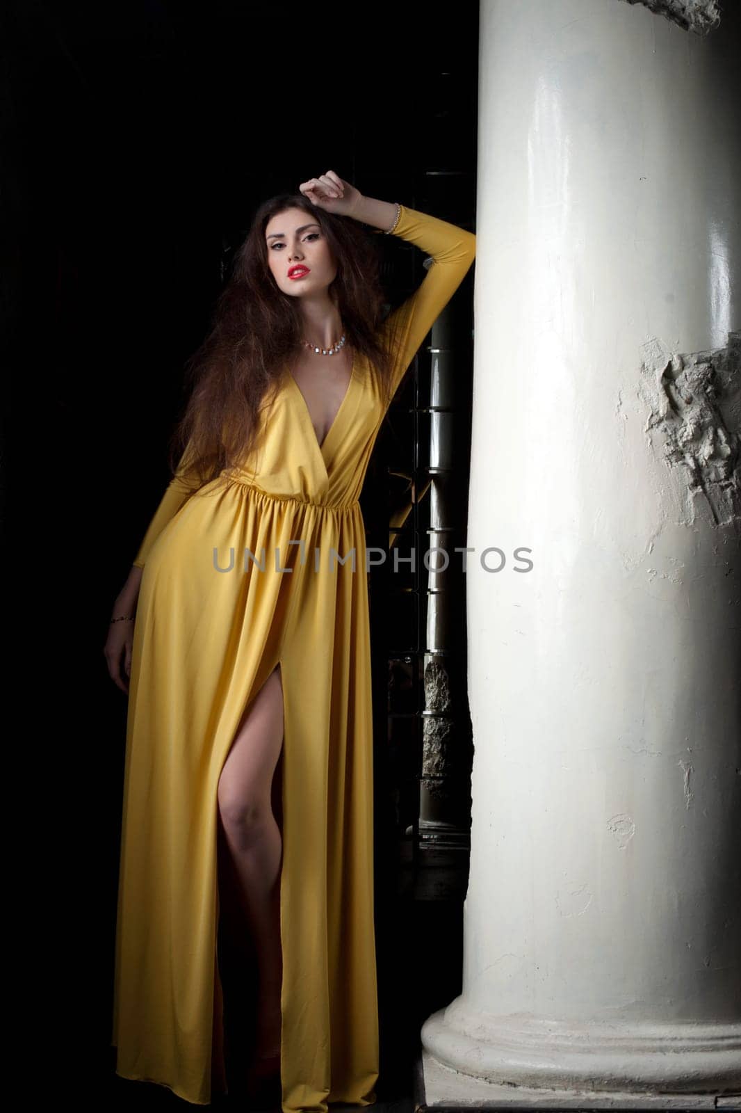 Portrait of beautiful brunette woman near column in fashion yellow dress
